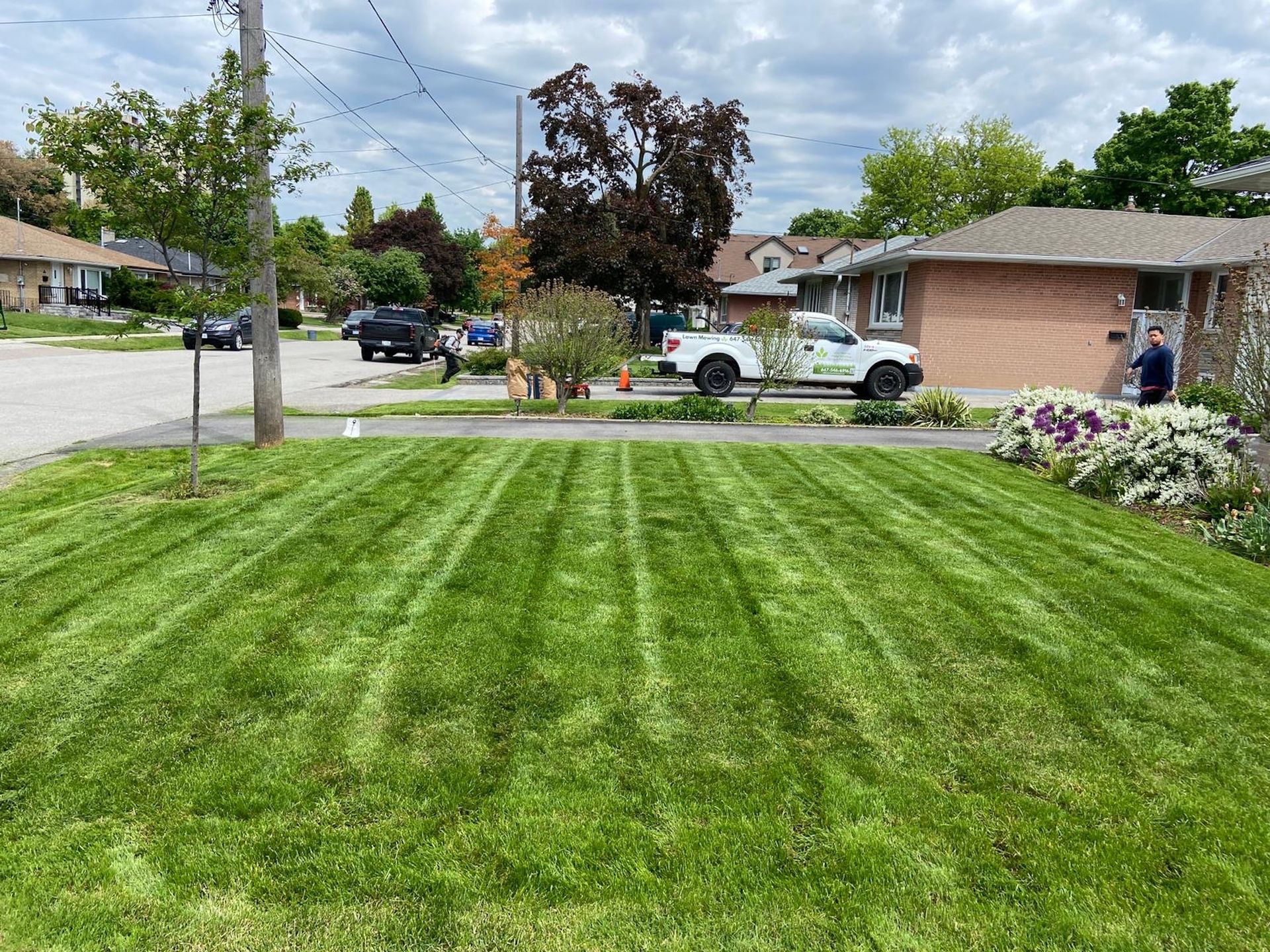 Lawn with distinct mowing stripes in front of a suburban house; a work truck is parked nearby.