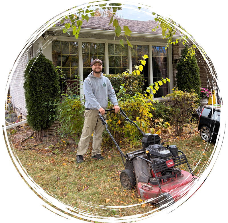 Man mowing a front yard with a red lawnmower beside a house and shrubs