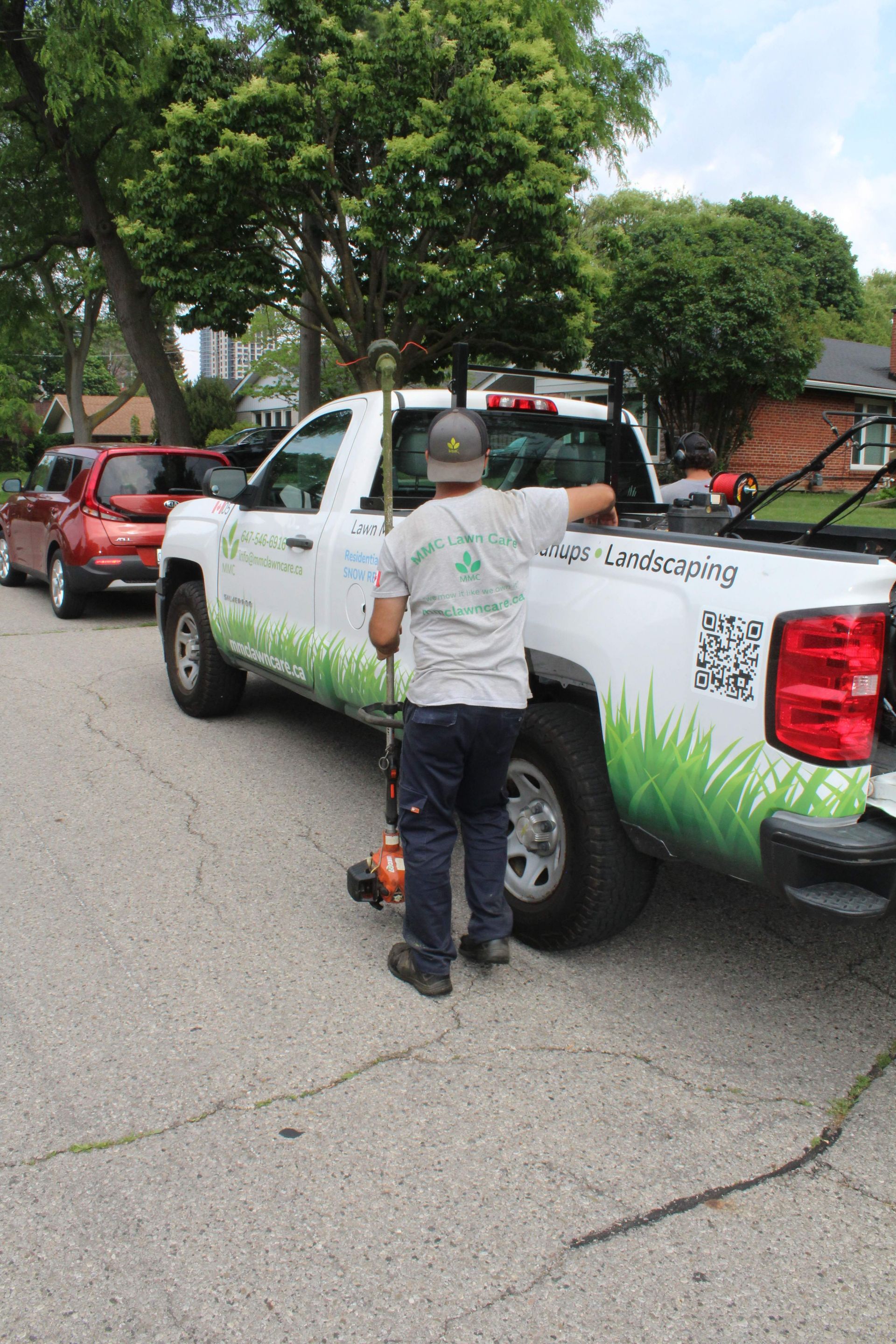 Worker fueling a white pickup truck with green graphics on a tree-lined street