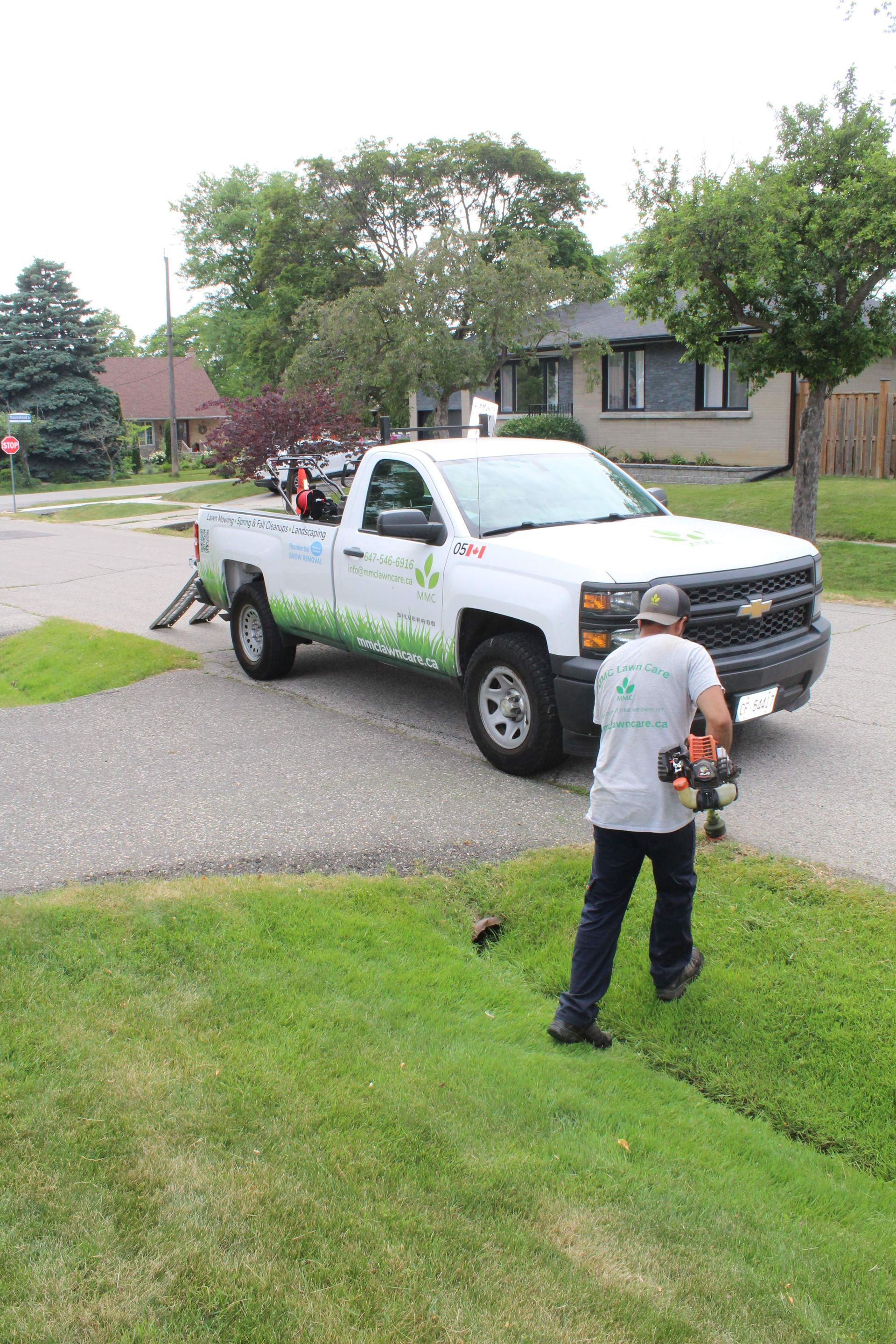 Man in gray shirt with camera facing white pickup truck on a suburban street, with another person in the truck.