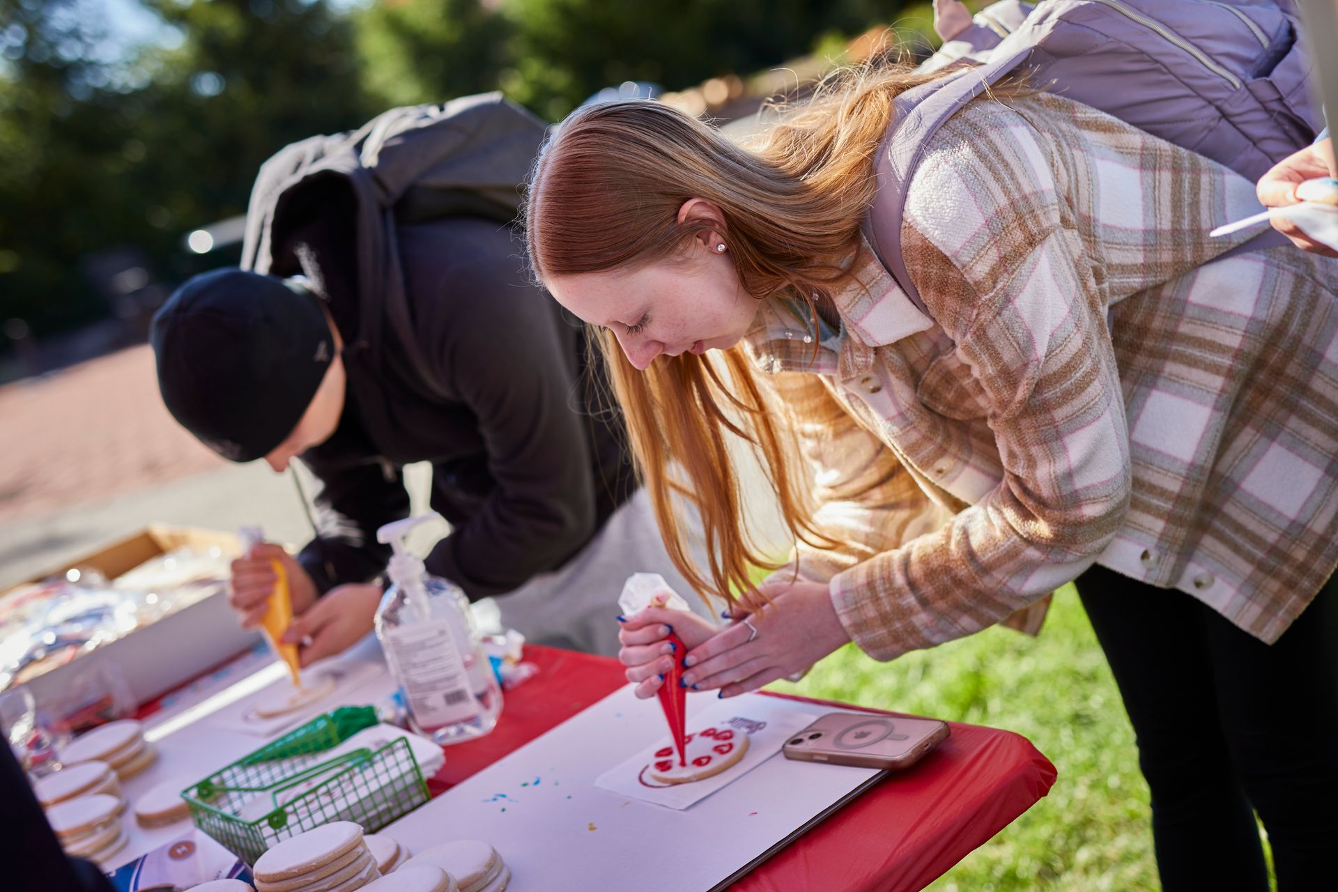 Two people bend over a table, writing on papers at an outdoor event.