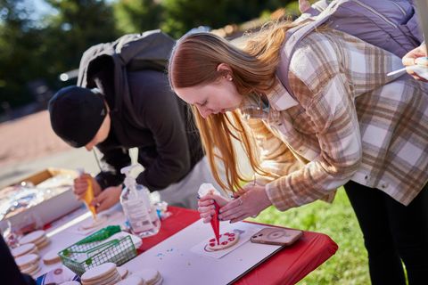 Two people bend over a table, writing on papers at an outdoor event.