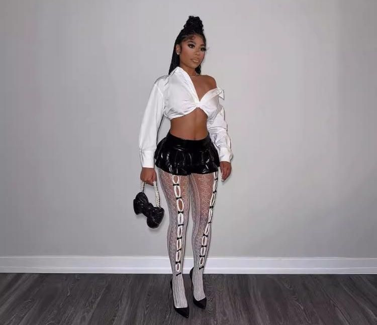 A woman is standing in a room wearing a white crop top and black shorts.