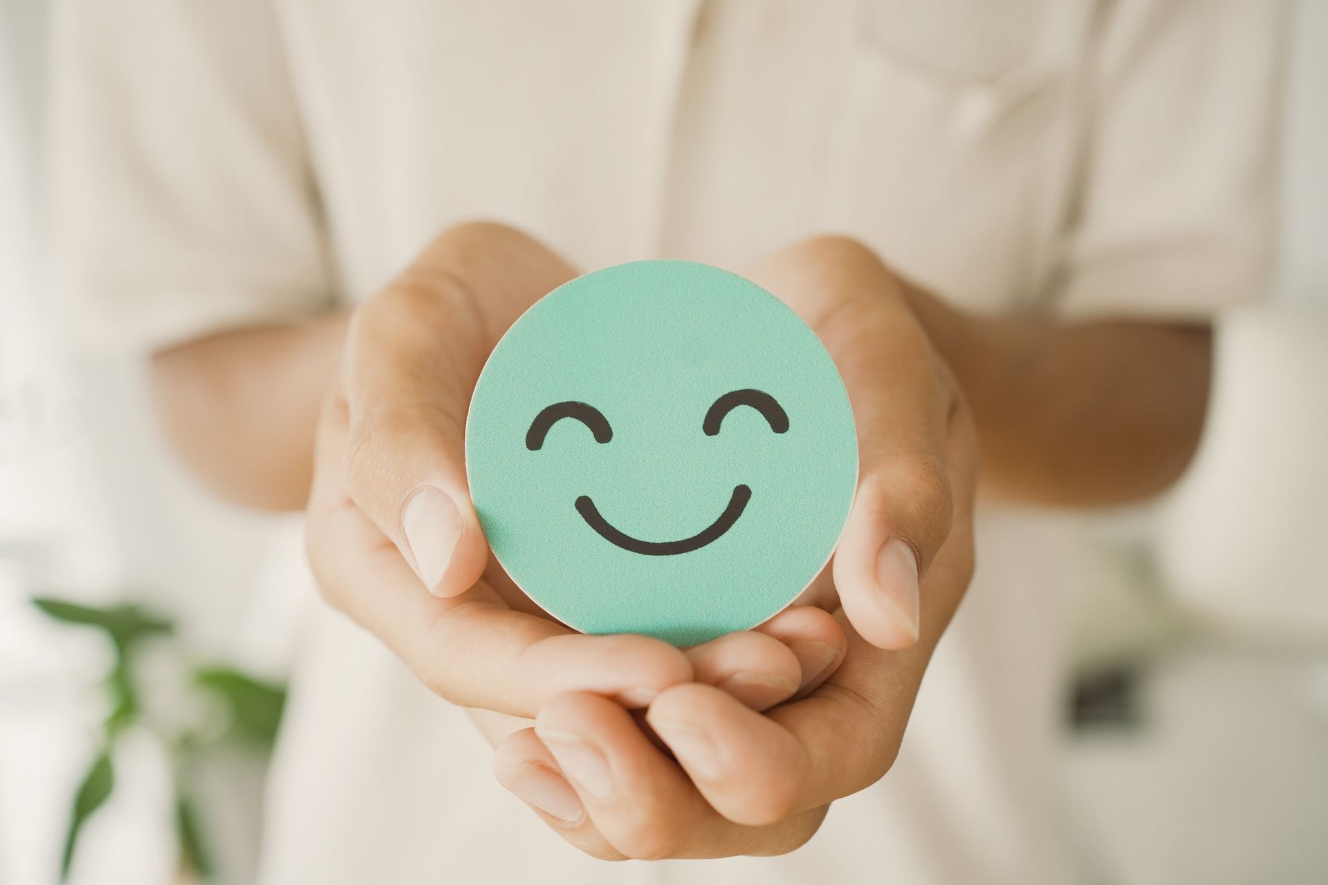Hands holding a light green circle with a smiling face drawn on it.