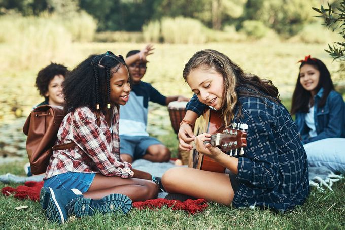 Group sitting on grass outdoors, smiling and playing guitar in a sunny field