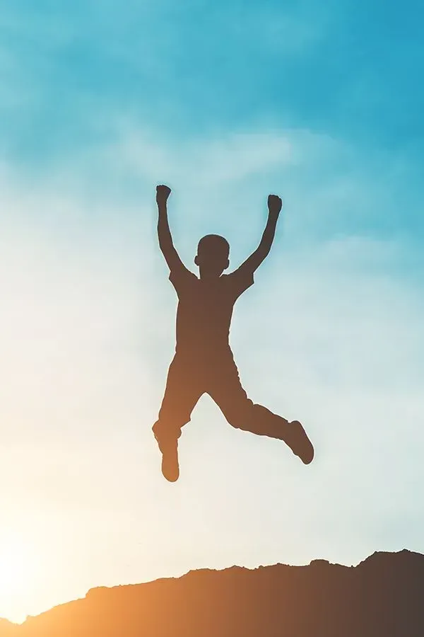A silhouette of a person jumping in the air with their arms in the air