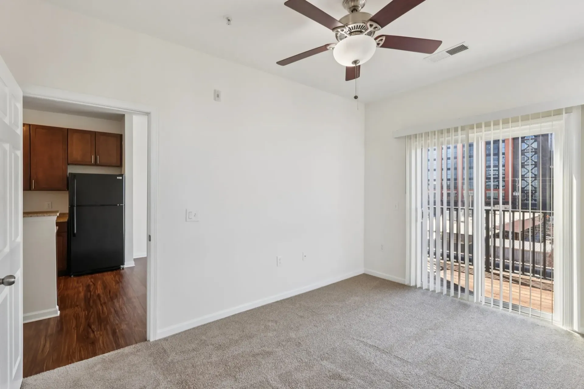 Living room with carpet, ceiling fan, and balcony access. Kitchen visible through doorway at Catherine 36 Apartments for rent in Charlotte, NC