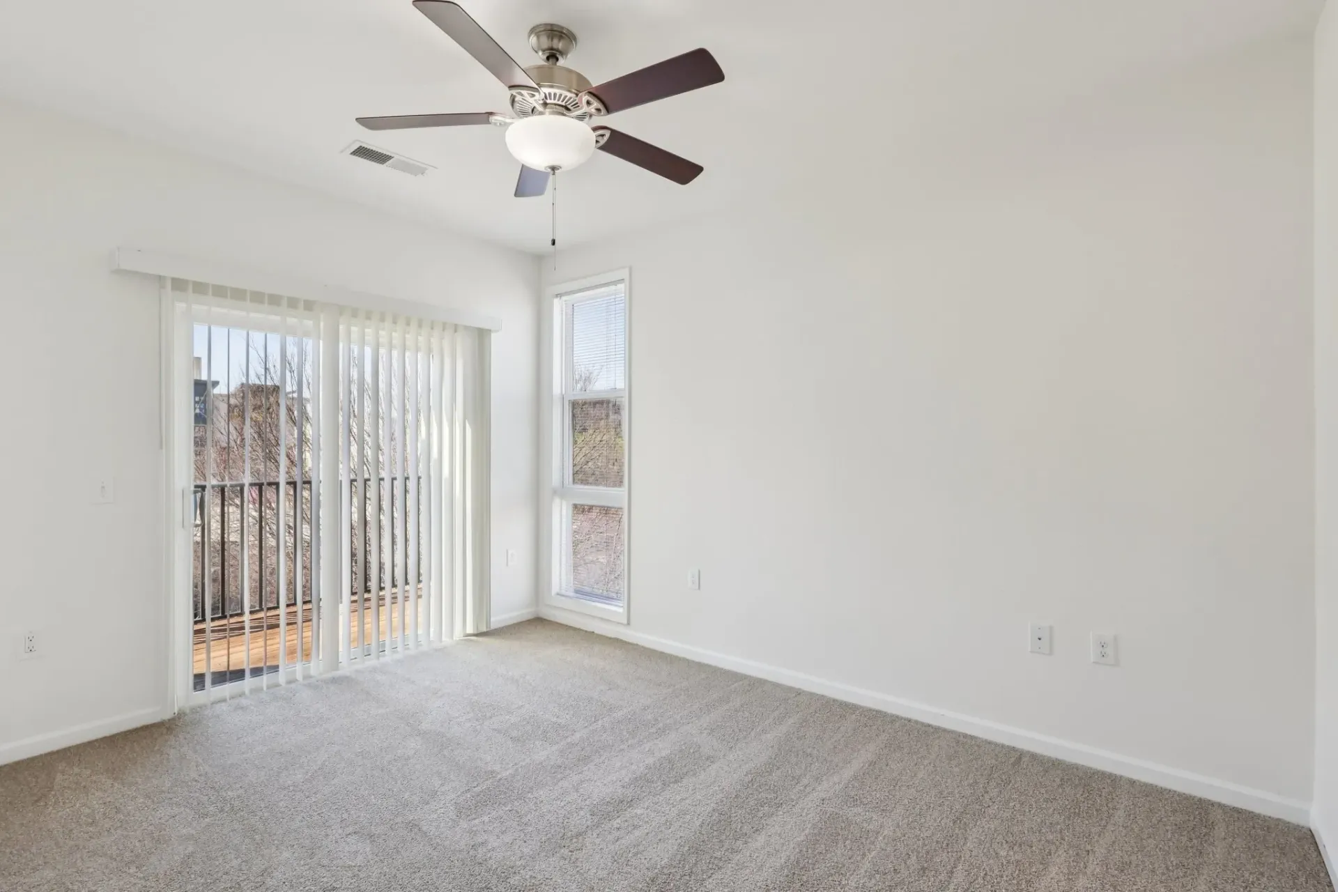 Empty apartment bedroom with neutral carpet, white walls, ceiling fan, and sliding glass doors to a balcony at Catherine 36 Apartments for rent in Charlotte, NC