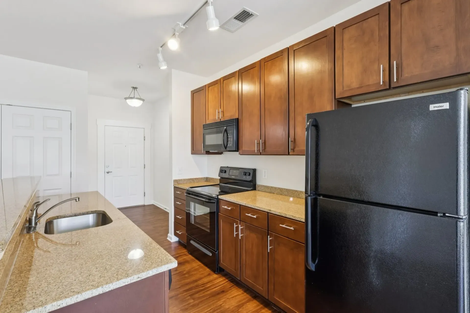 Kitchen with granite countertops, stainless steel sink, wooden cabinets, black appliances, and a doorway at Catherine 36 Apartments for rent in Charlotte, NC