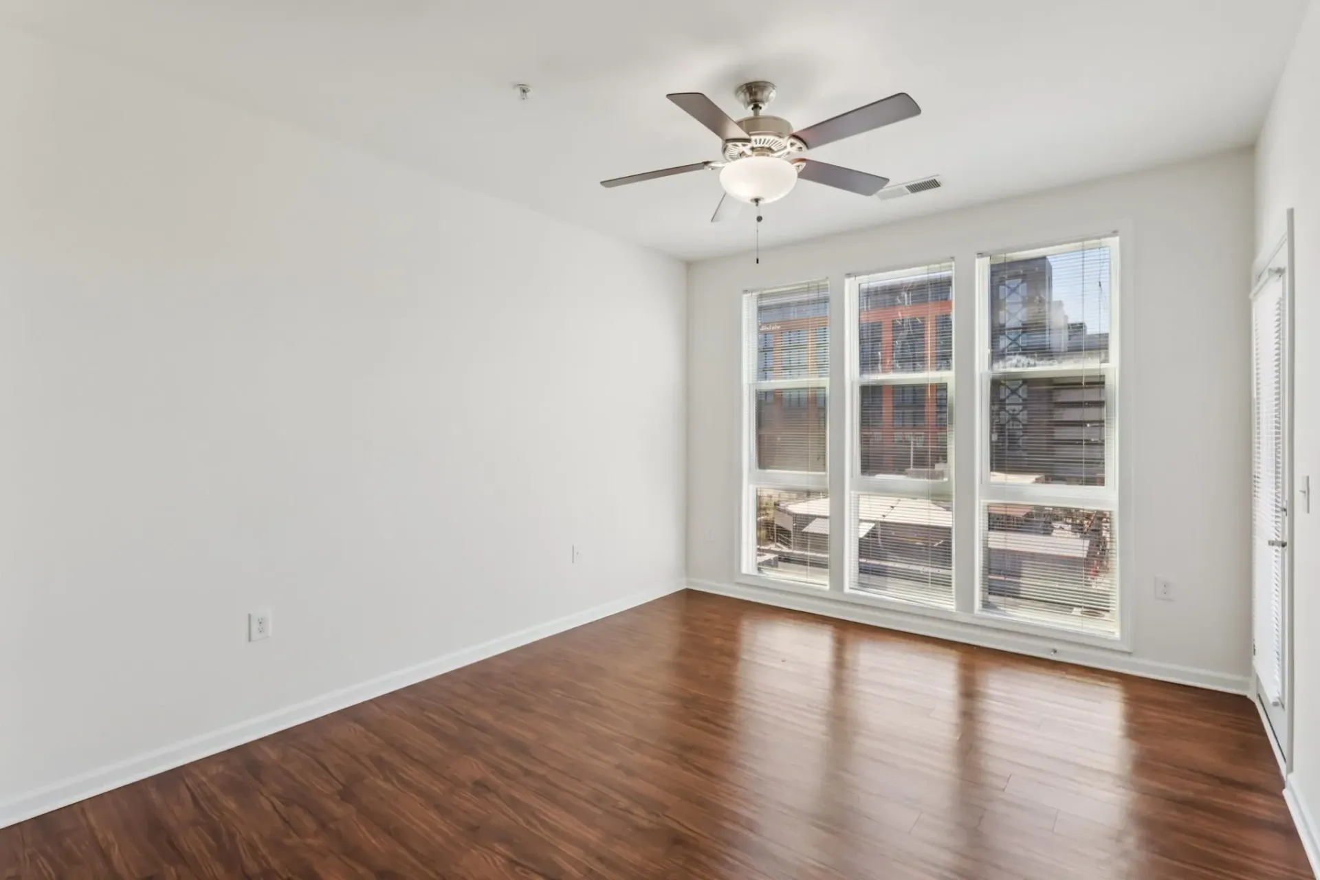 Empty living room with hardwood floors, a ceiling fan, and large windows overlooking the city at Catherine 36 Apartments for rent in Charlotte, NC