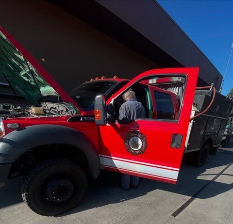 Red fire truck with open door at a station, a person standing beside it under a canopy