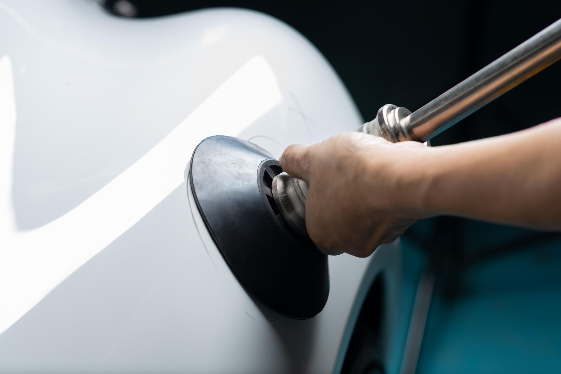 Hand pushing a suction cup on a white car dent for paintless dent repair