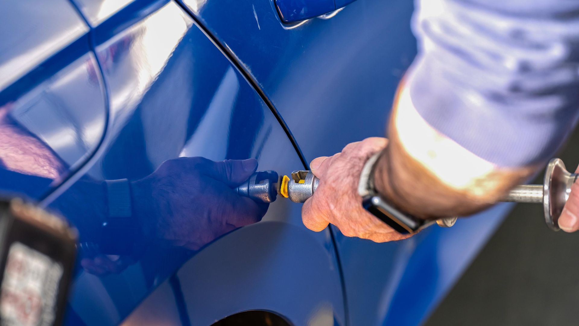Person using a handheld buffer to polish a blue car door