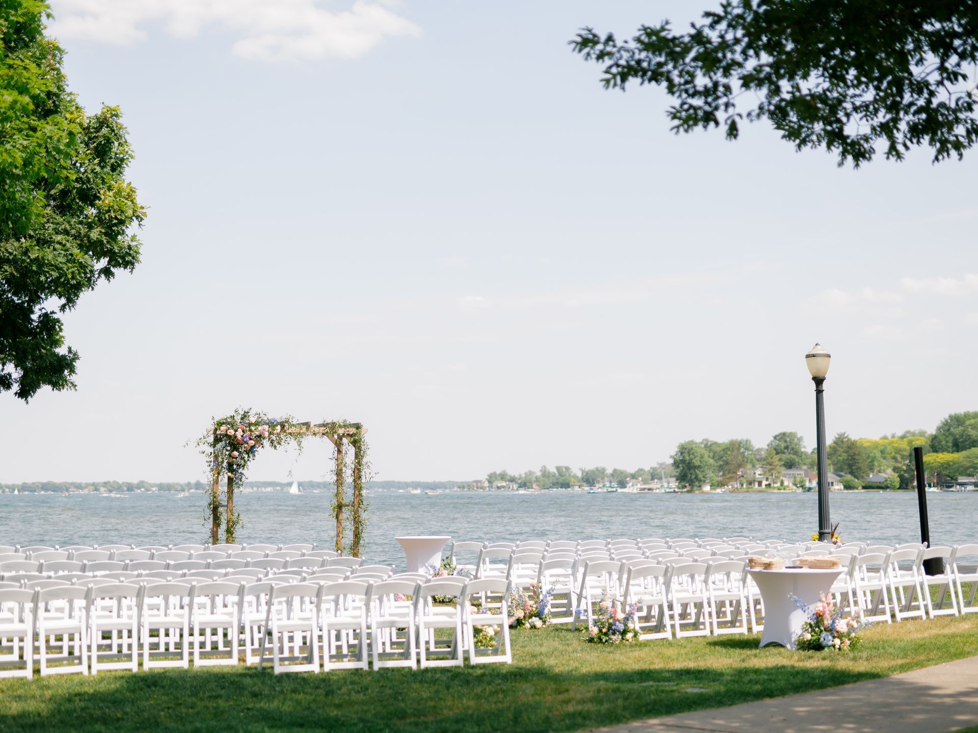 A row of white chairs are lined up in front of a lake for a wedding ceremony.