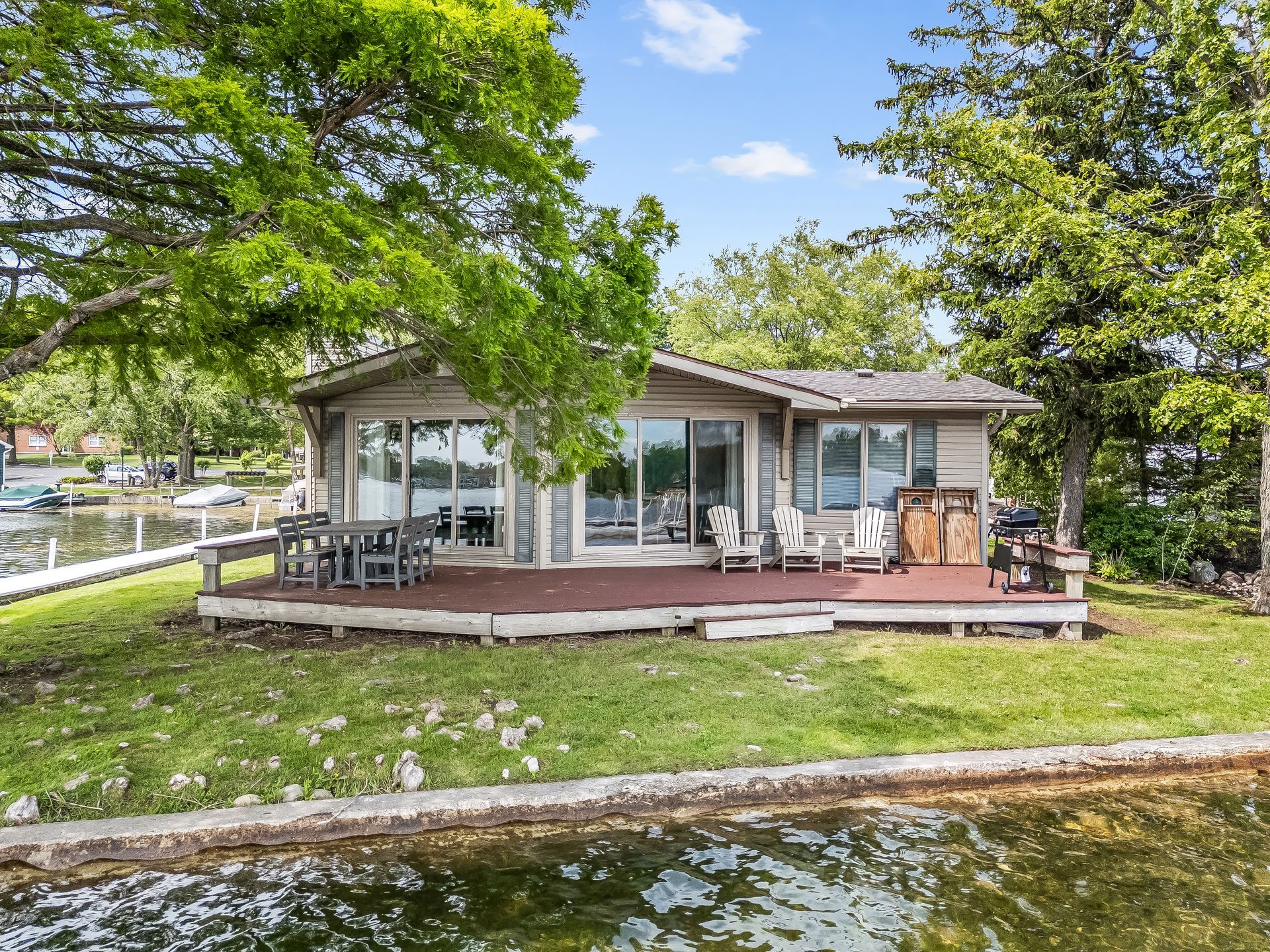 A house with a large deck is sitting on the shore of a lake.