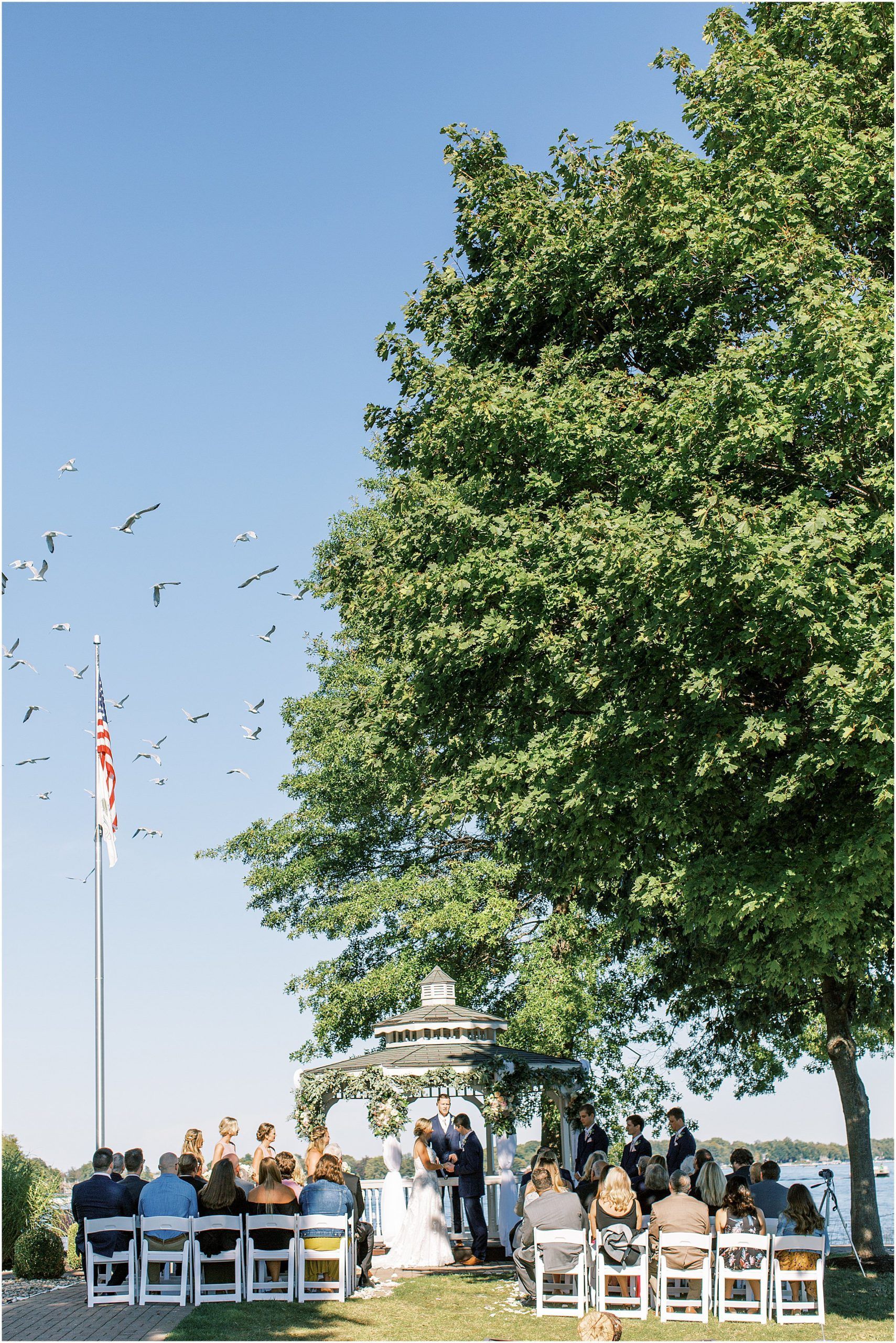 A bride and groom are getting married under a gazebo in front of a large tree.