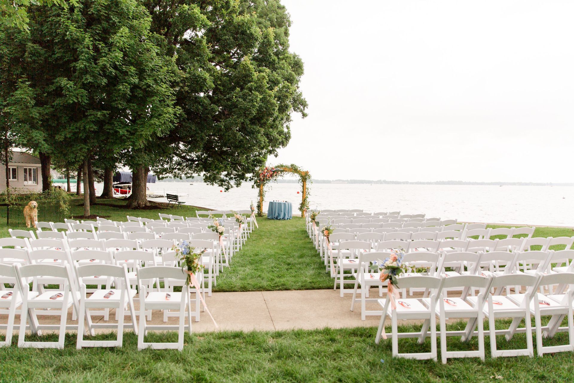 A row of white chairs are lined up in front of a lake for a wedding ceremony.