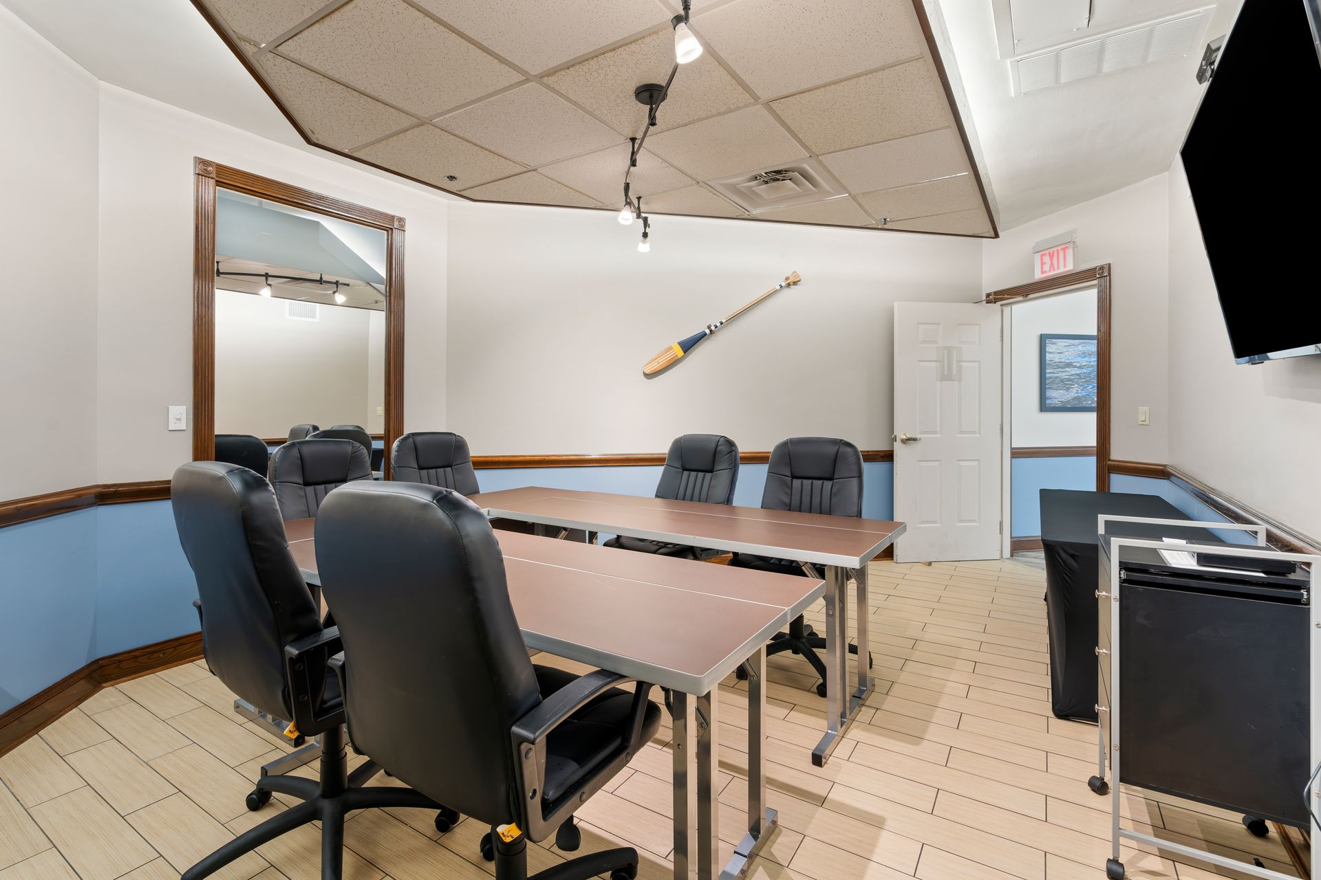 A conference room with tables and chairs and a television on the wall.