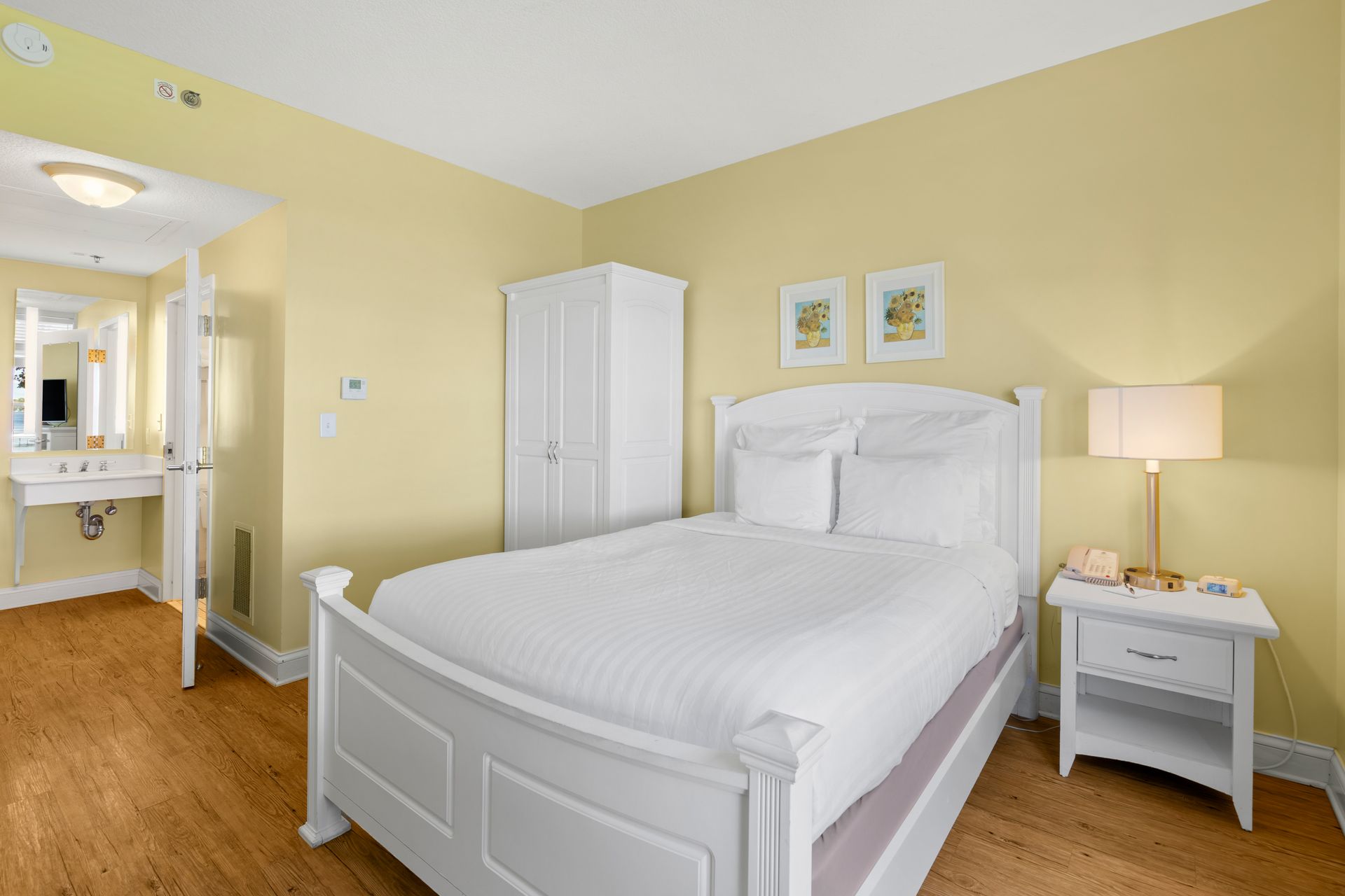 A hotel room with a king size bed , nightstand , lamp and wardrobe.