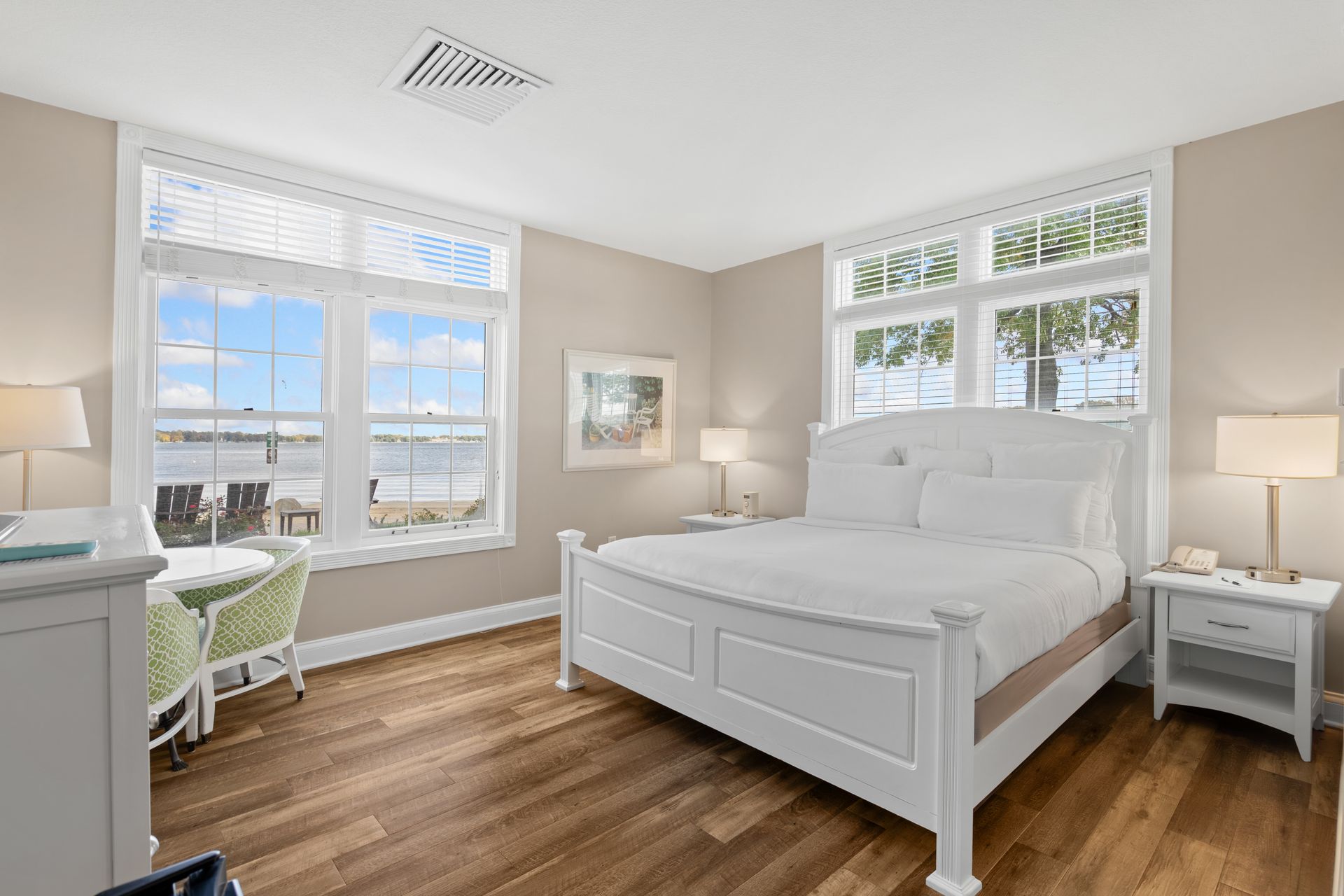 A bedroom with a king size bed , two nightstands , a desk and two windows.