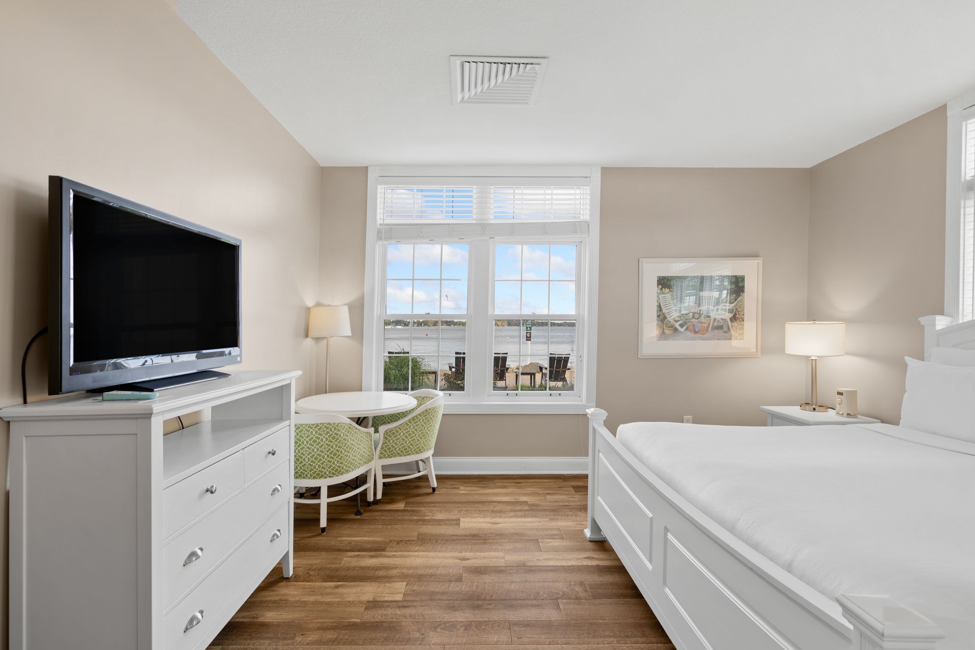 A bedroom with a king size bed , television , dresser and chairs.