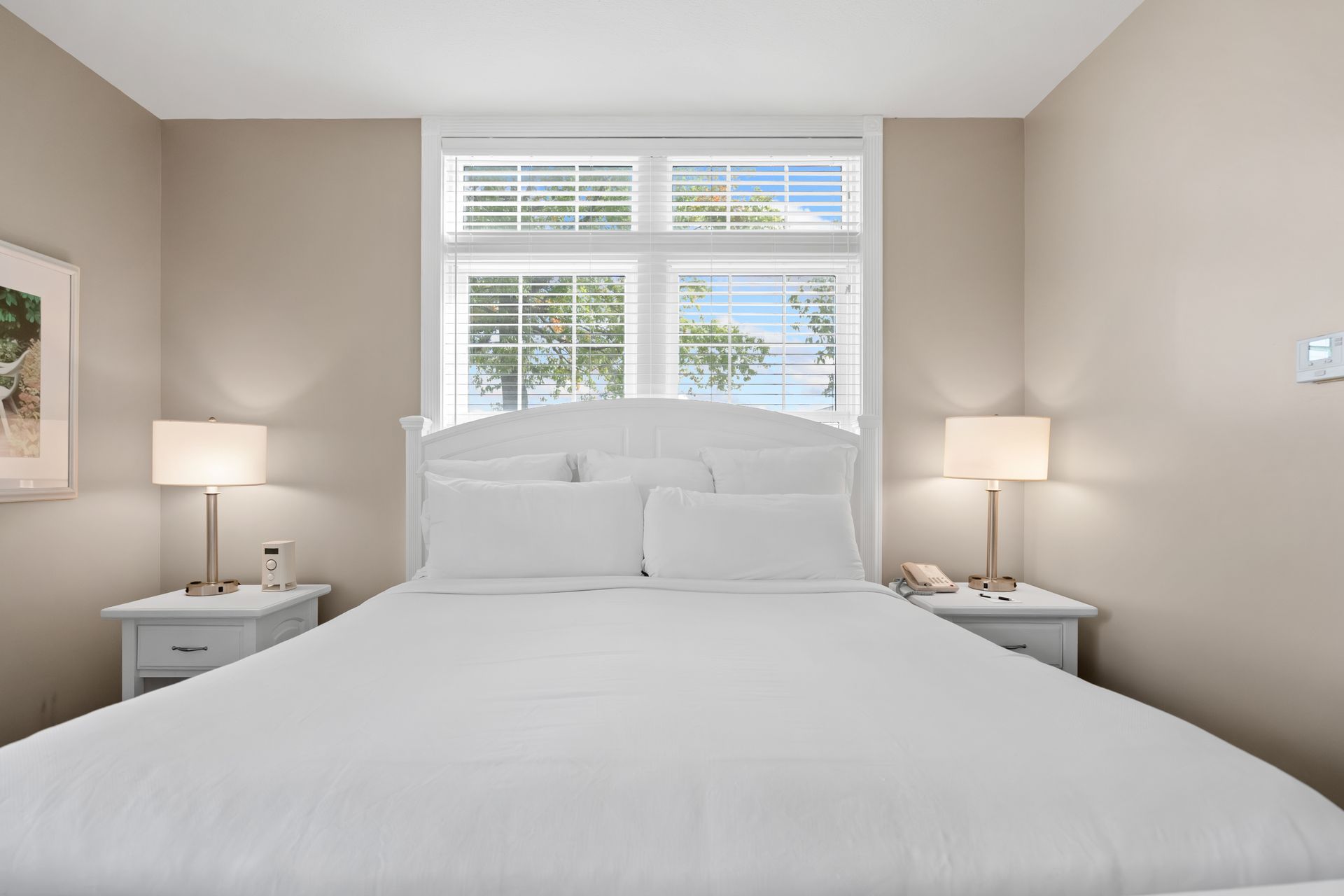 A bedroom with a king size bed , two nightstands , two lamps and a window.