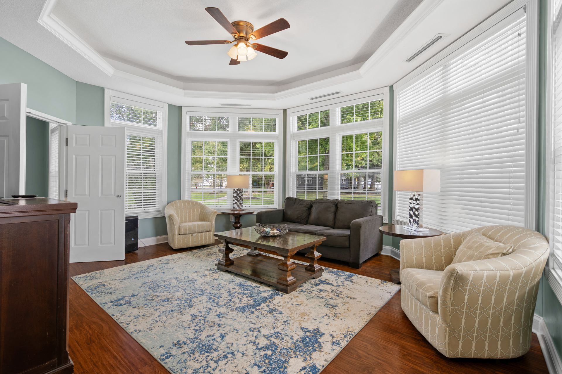 A living room with a couch , chairs , a coffee table and a ceiling fan.