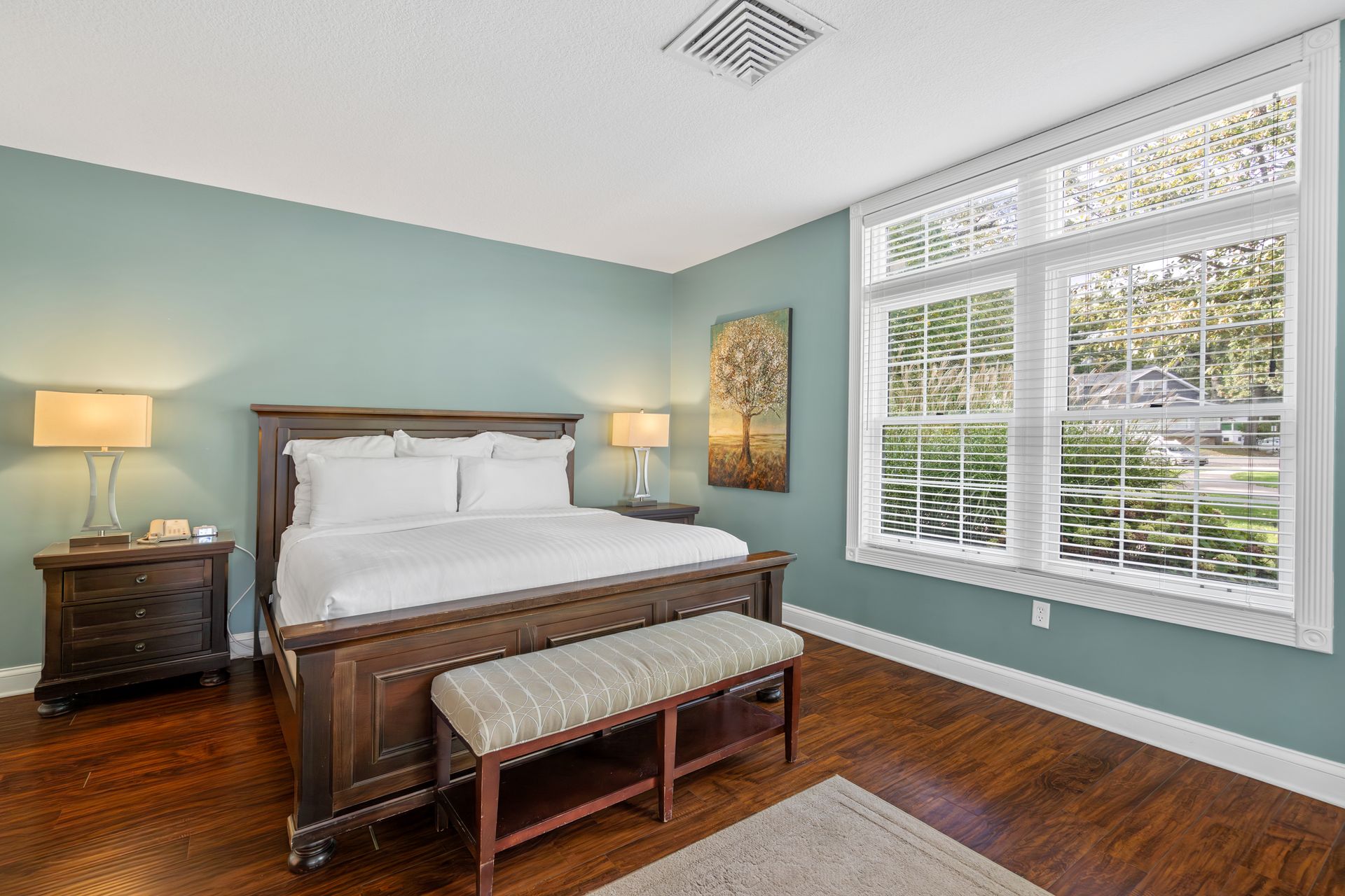 A bedroom with a king size bed , nightstands , lamps , and a bench.