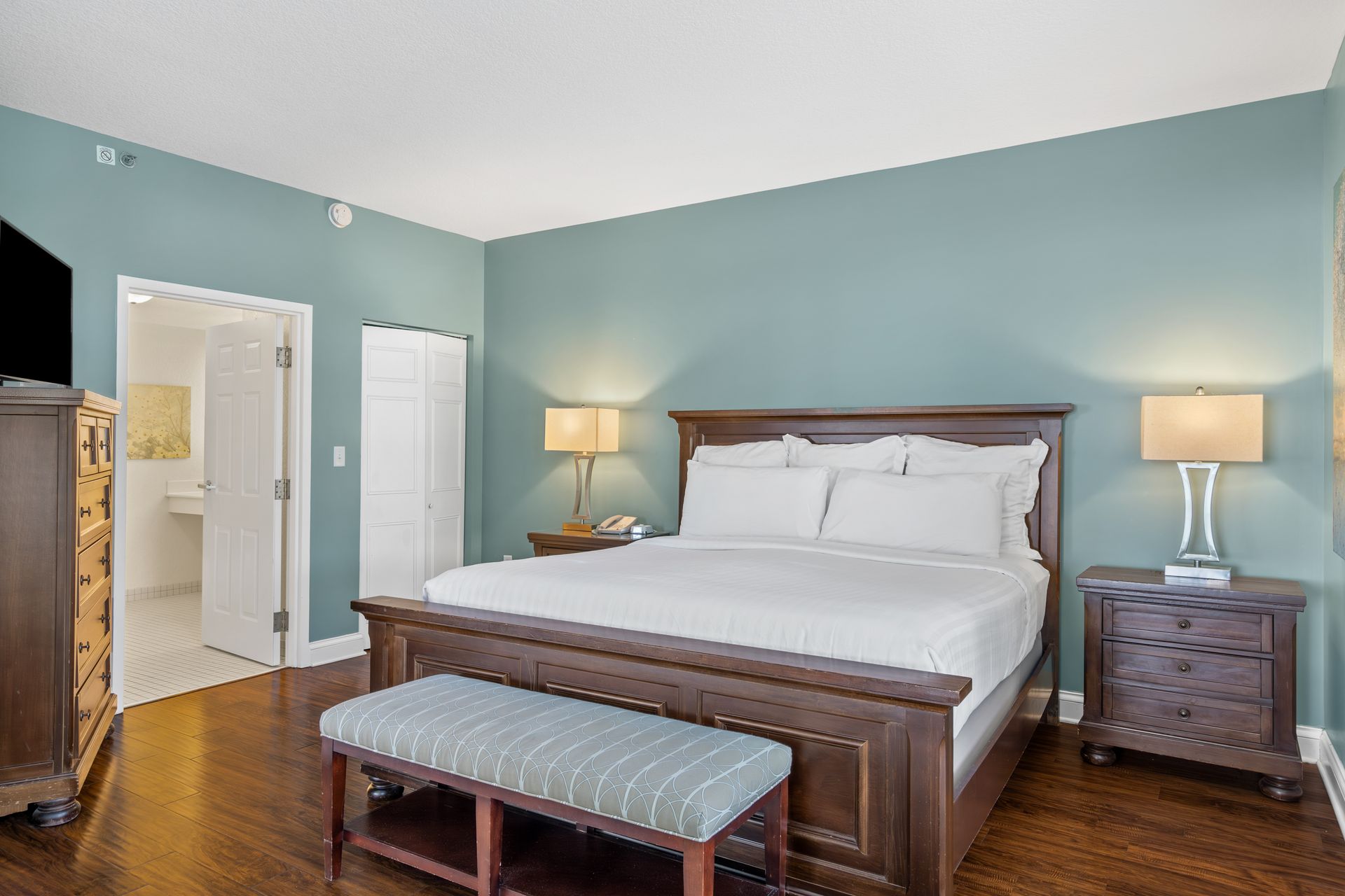 A bedroom with a king size bed , nightstands , lamps and a bench.