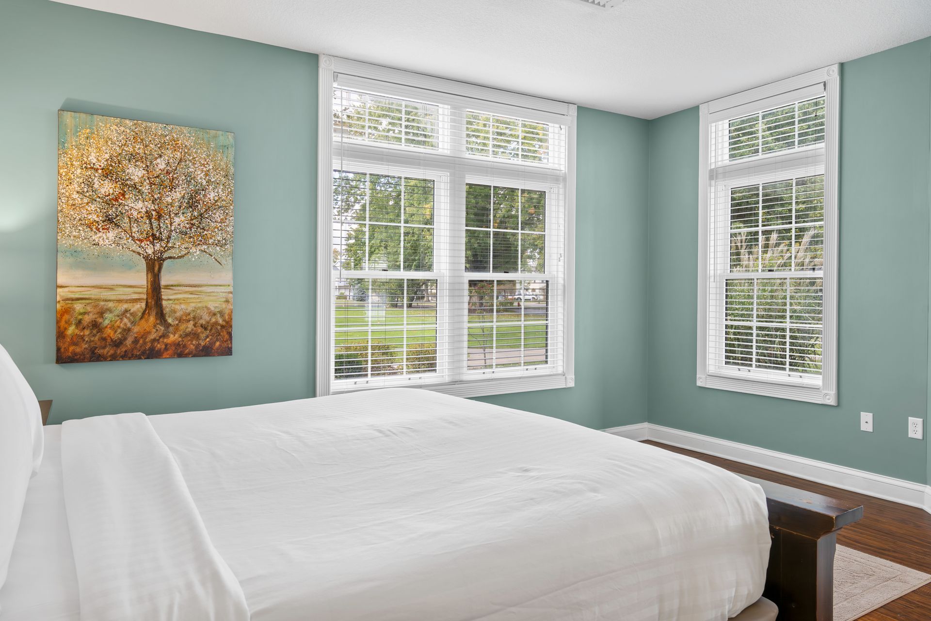 There is a painting of a tree on the wall above the bed in the bedroom.