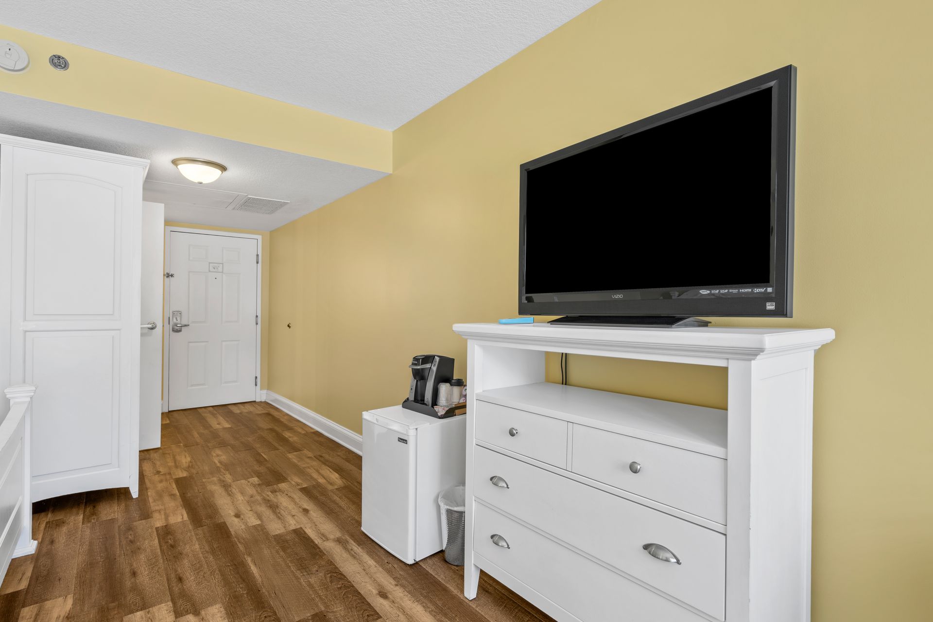 A hotel room with a flat screen tv on a dresser.