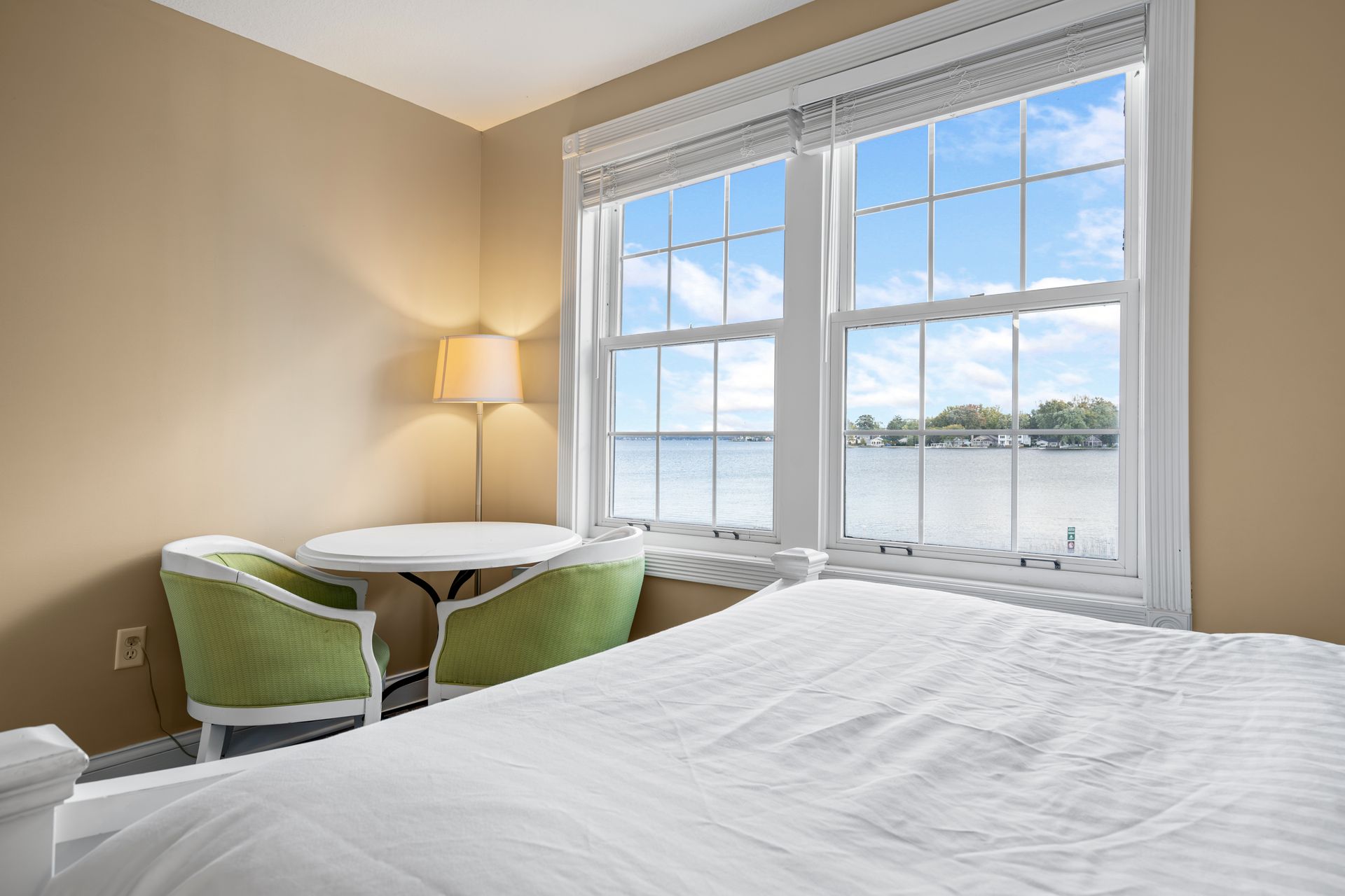 A bedroom with a bed , chairs , table and window with a view of the water.