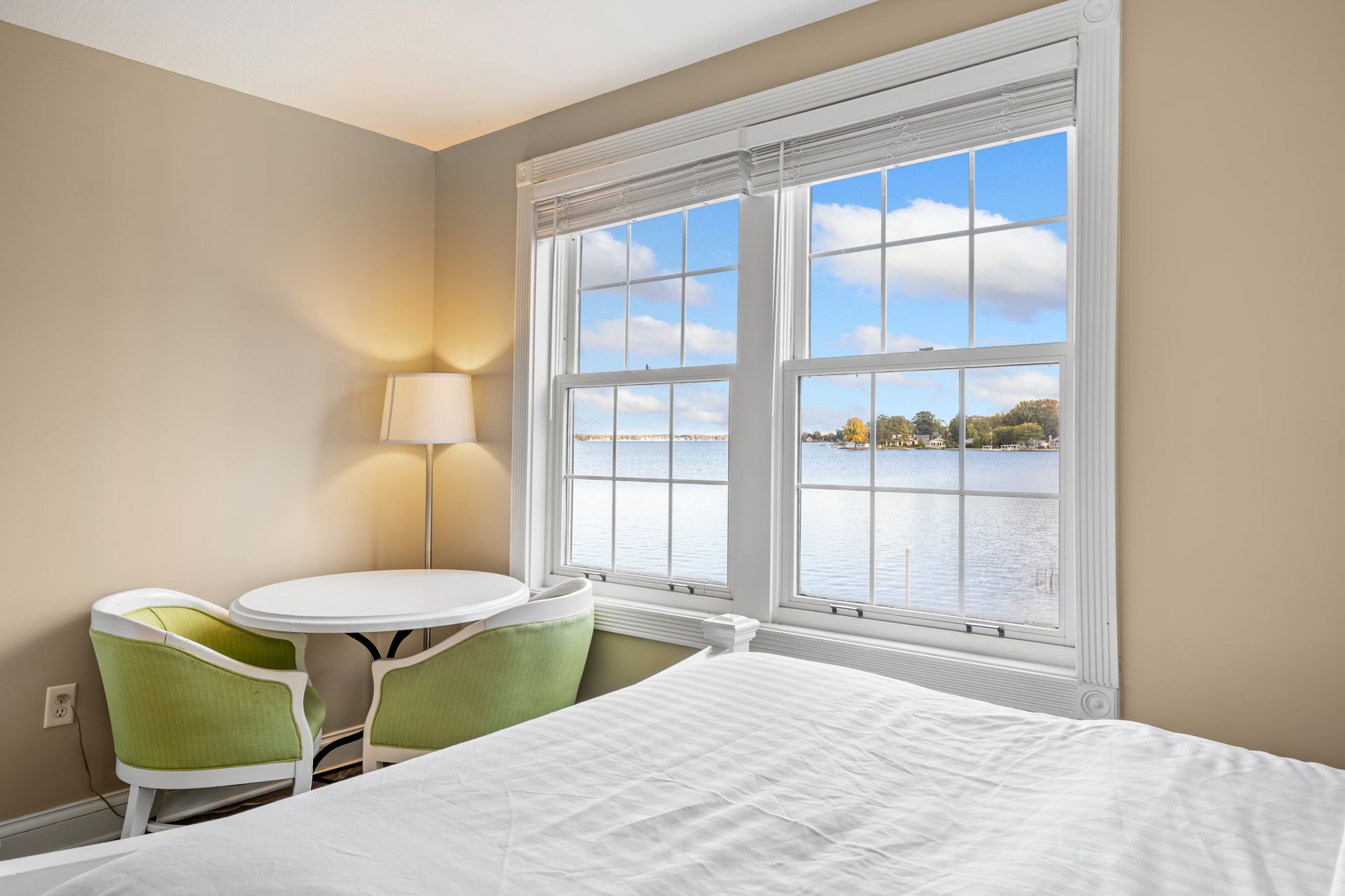 A bedroom with a bed , table , chairs and a window with a view of a lake.