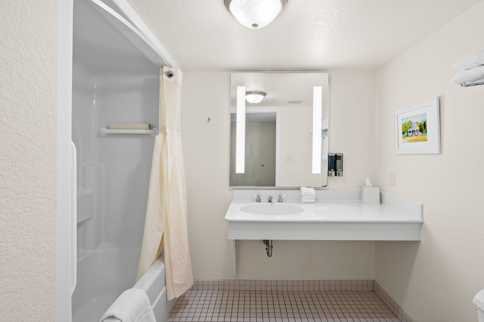 A bathroom in a hotel room with a tub , sink and mirror.