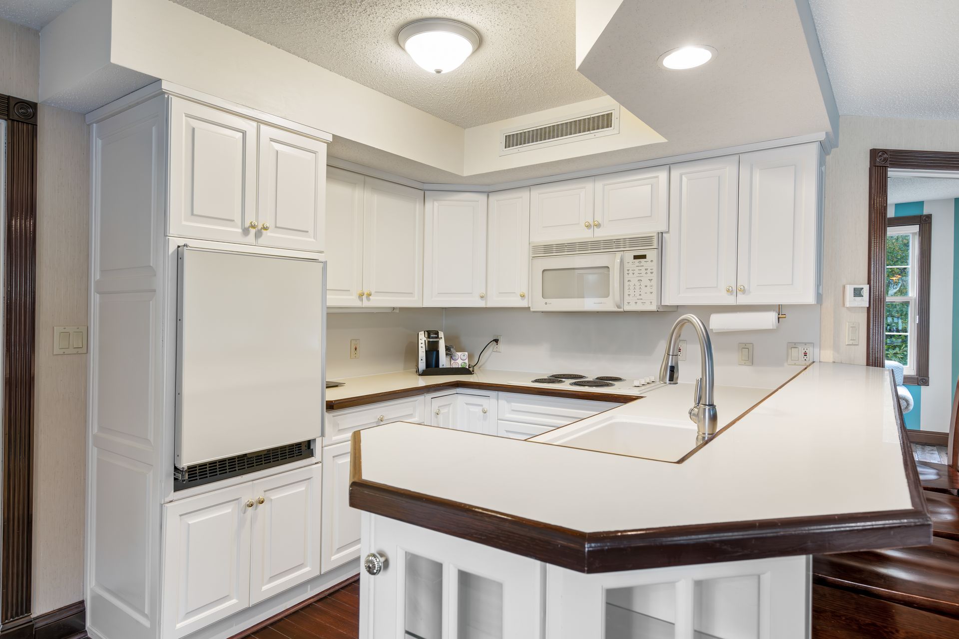 A kitchen with white cabinets , a sink , a refrigerator , and a microwave.