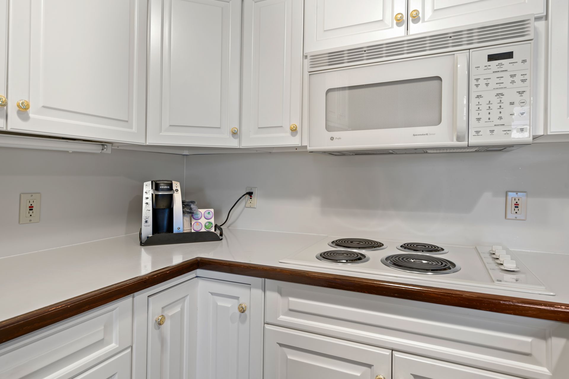 A kitchen with white cabinets , a stove , a microwave , and a coffee maker.