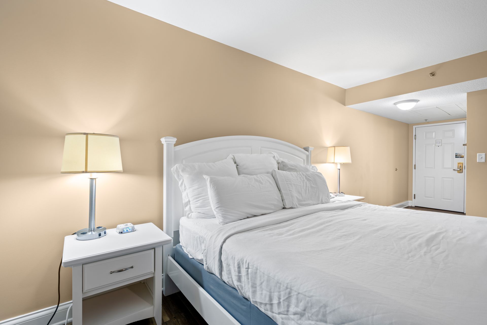 A bedroom with a bed , nightstand , lamp and door.