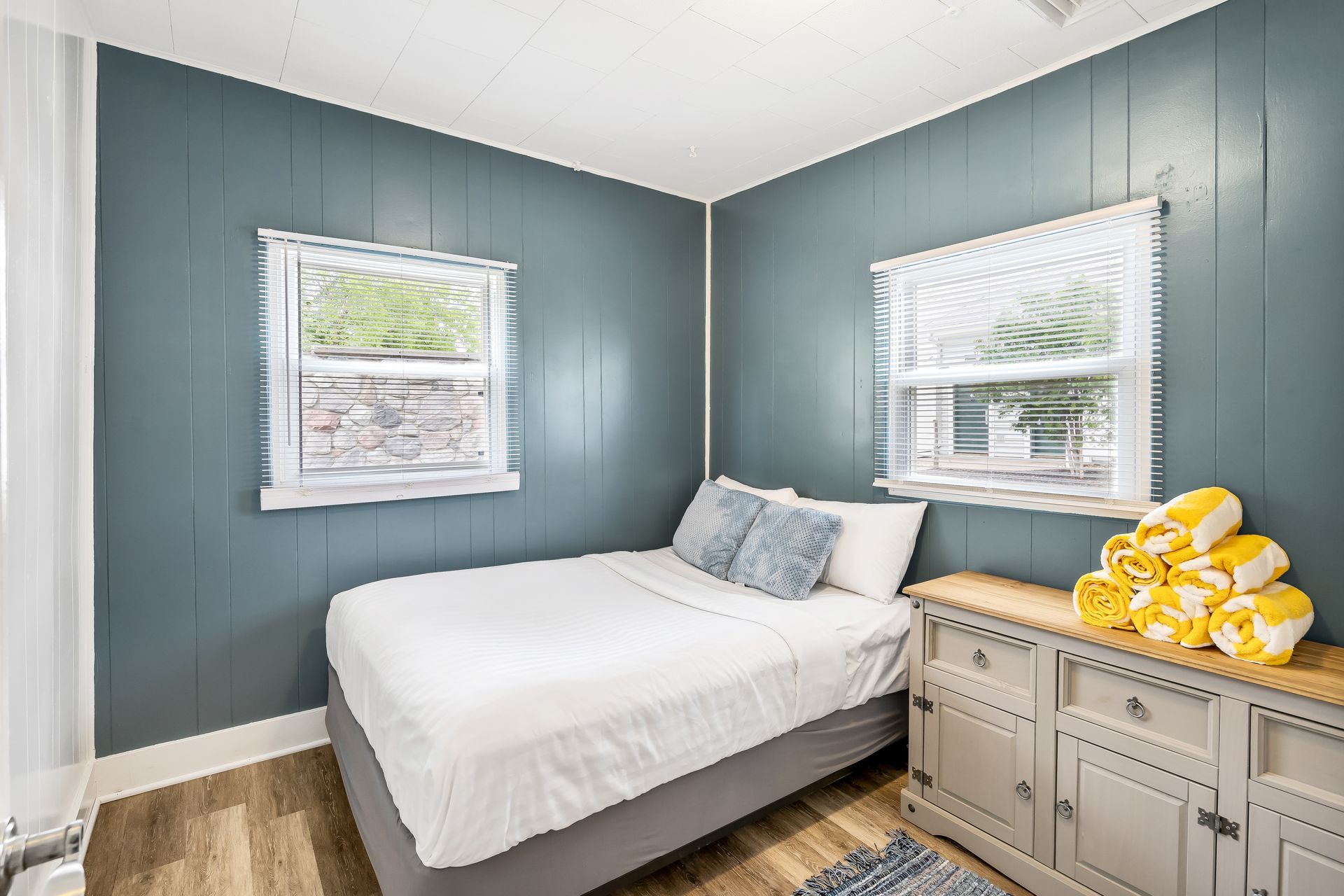 A bedroom with a bed , dresser , and two windows.