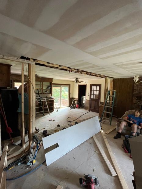 Renovation work in a room with exposed walls, tools, and a worker crouching on the right