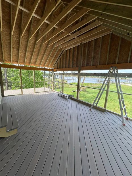 Interior of an unfinished house with exposed roof framing, gray floor, and a ladder by open walls overlooking greenery