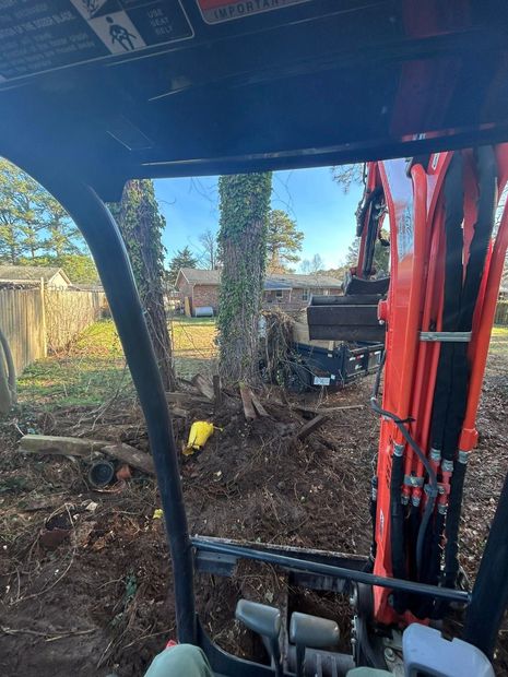 Red excavator arm digging soil in a backyard with a covered structure overhead