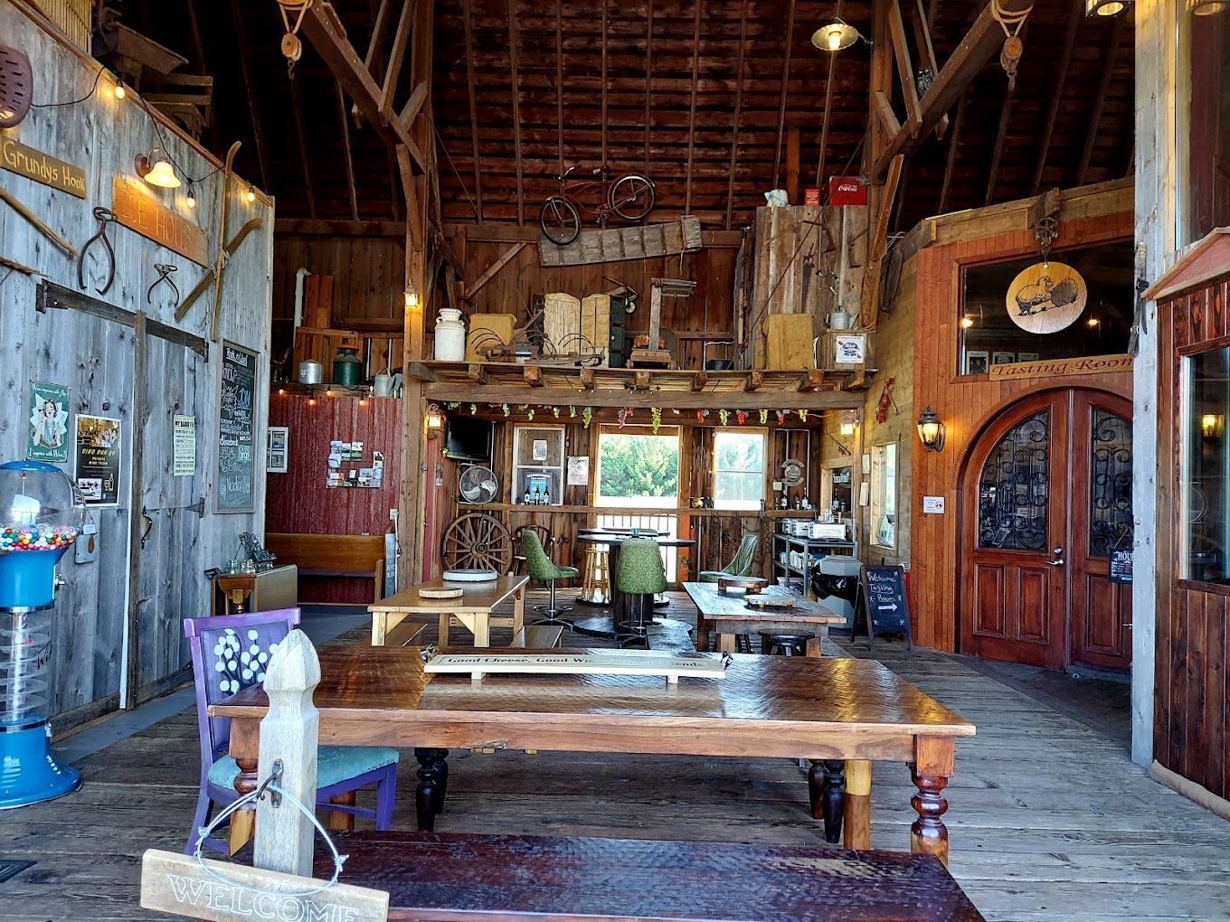 Interior of a rustic barn with tables, seating, and decorative items. Natural light streams in; wood tones dominate.