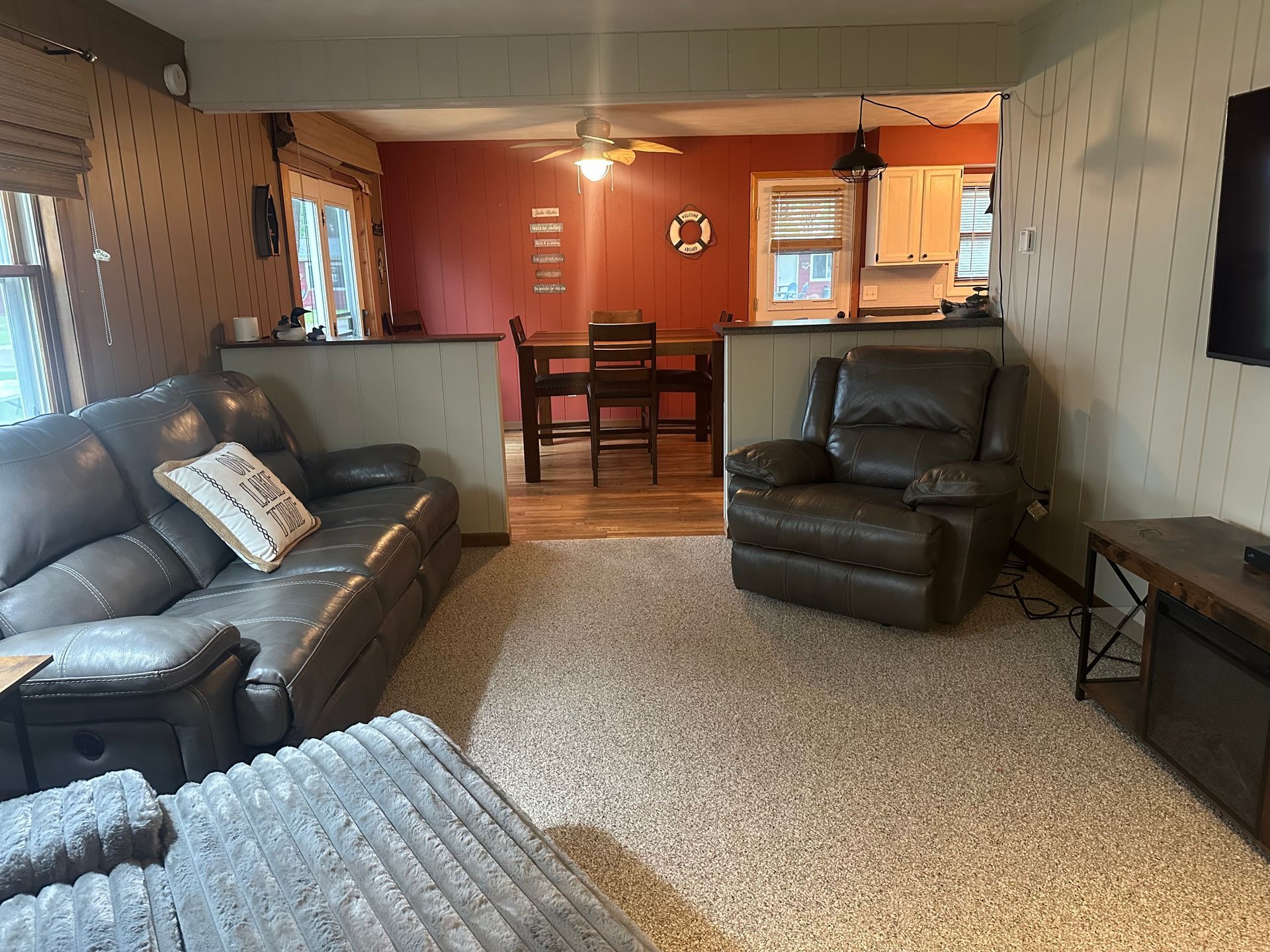 Living room with gray sofa and recliner, carpet, and an opening to the dining area and kitchen.