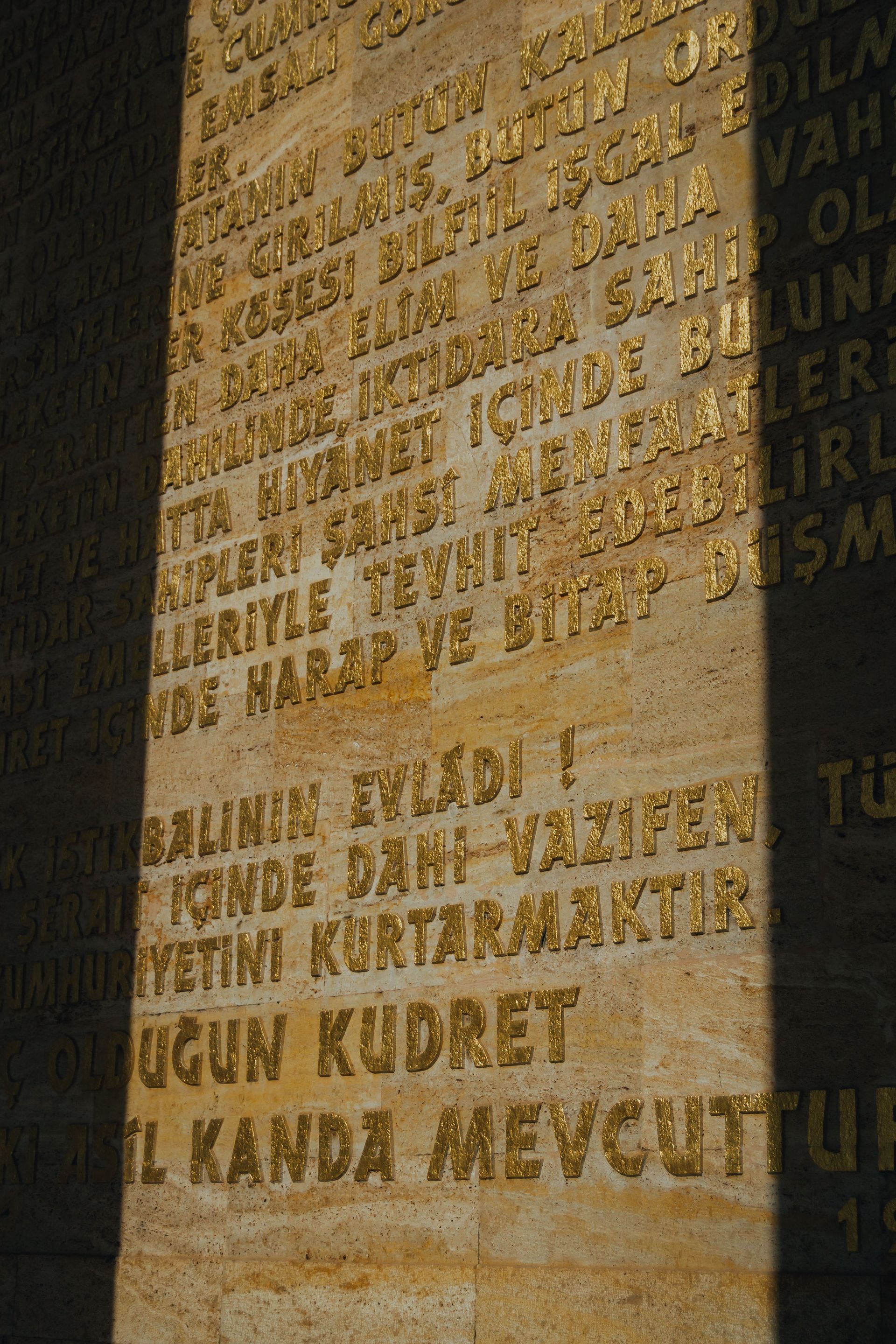 Close-up of a stone wall with engraved Turkish text in gold and shadow