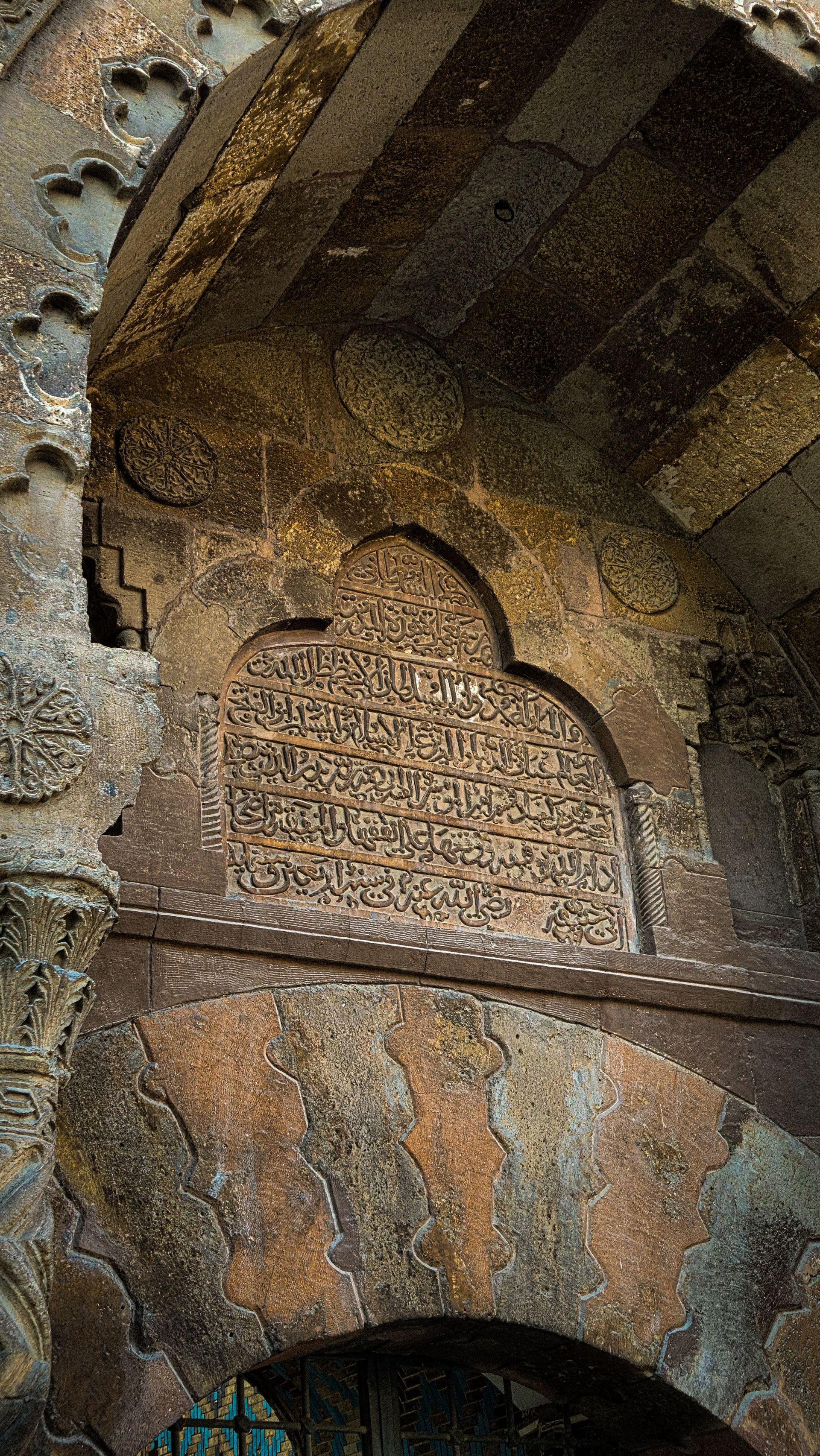 Carved stone wall with a framed Arabic inscription beneath an arched ceiling in warm brown tones