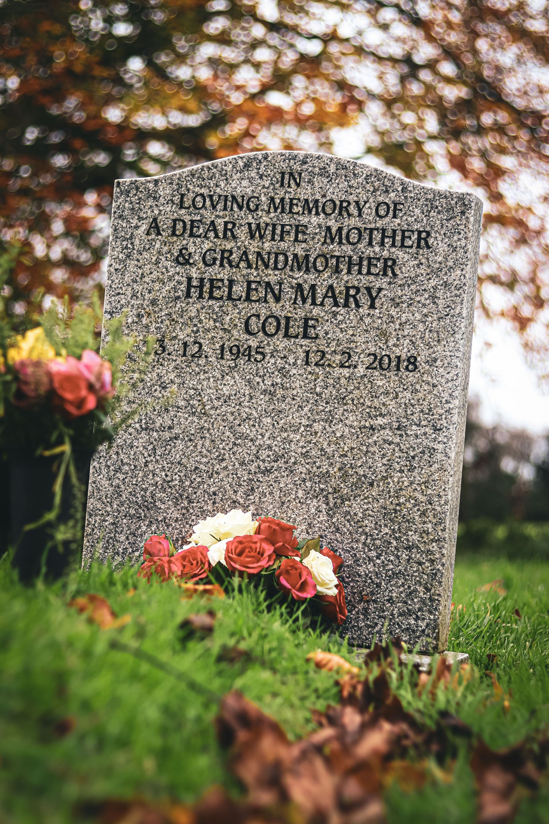 Gravestone in a cemetery with pink and orange flowers at its base