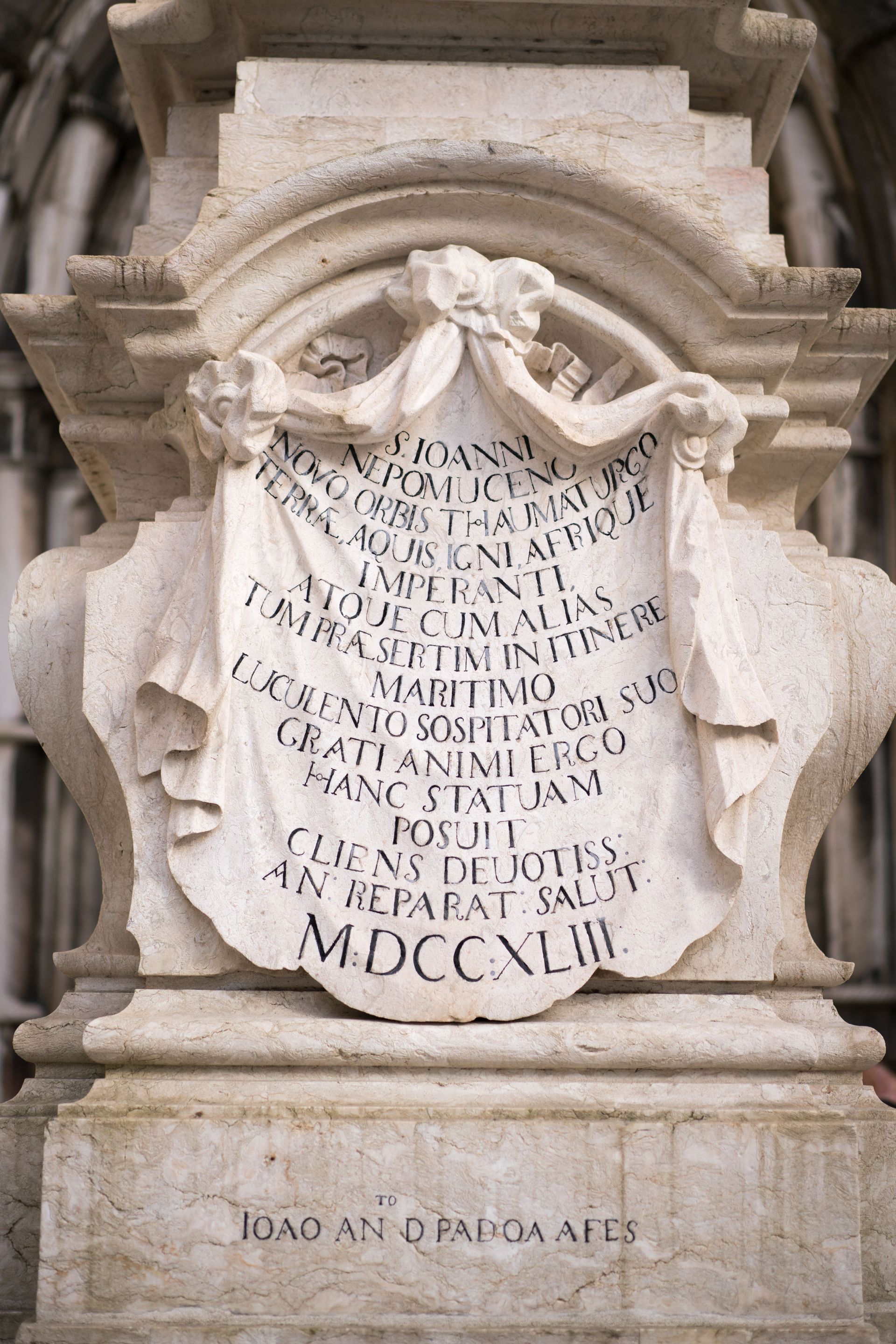 Inscribed white marble memorial plaque with Latin text set into an ornate stone wall