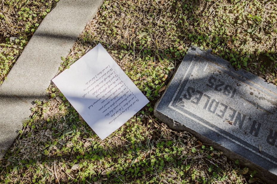 White paper and carved stone marker on sunlit grass beside a concrete path.
