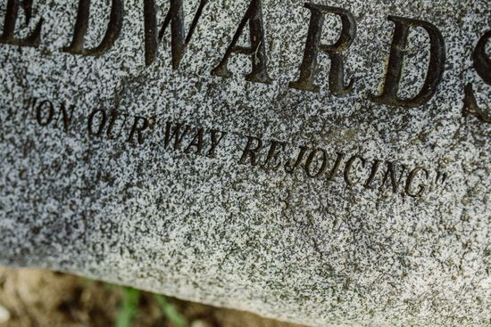 Close-up of a weathered engraved stone marker with faint inscription on gray granite.
