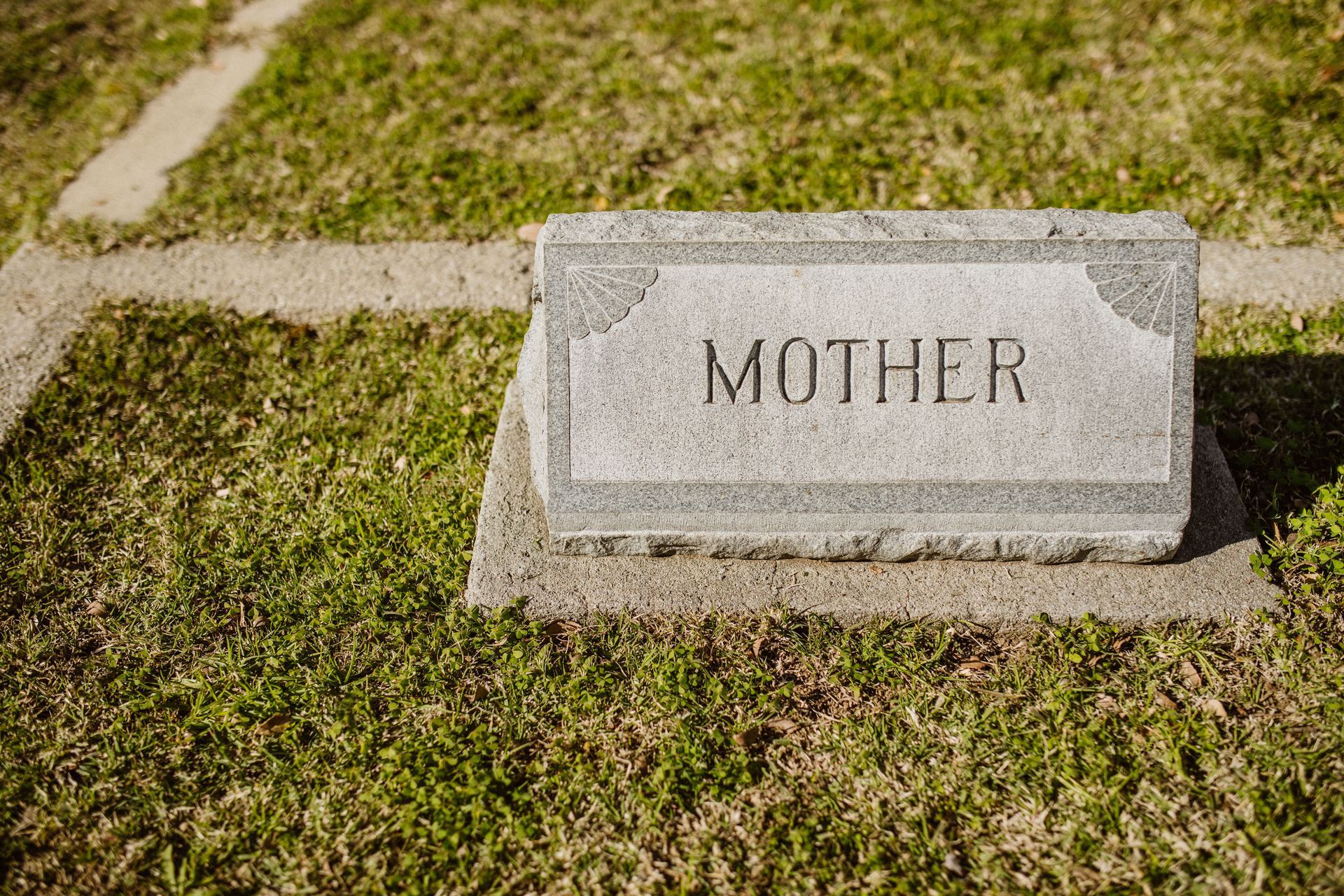 Gravestone marker engraved “MOTHER” on a grassy cemetery plot.